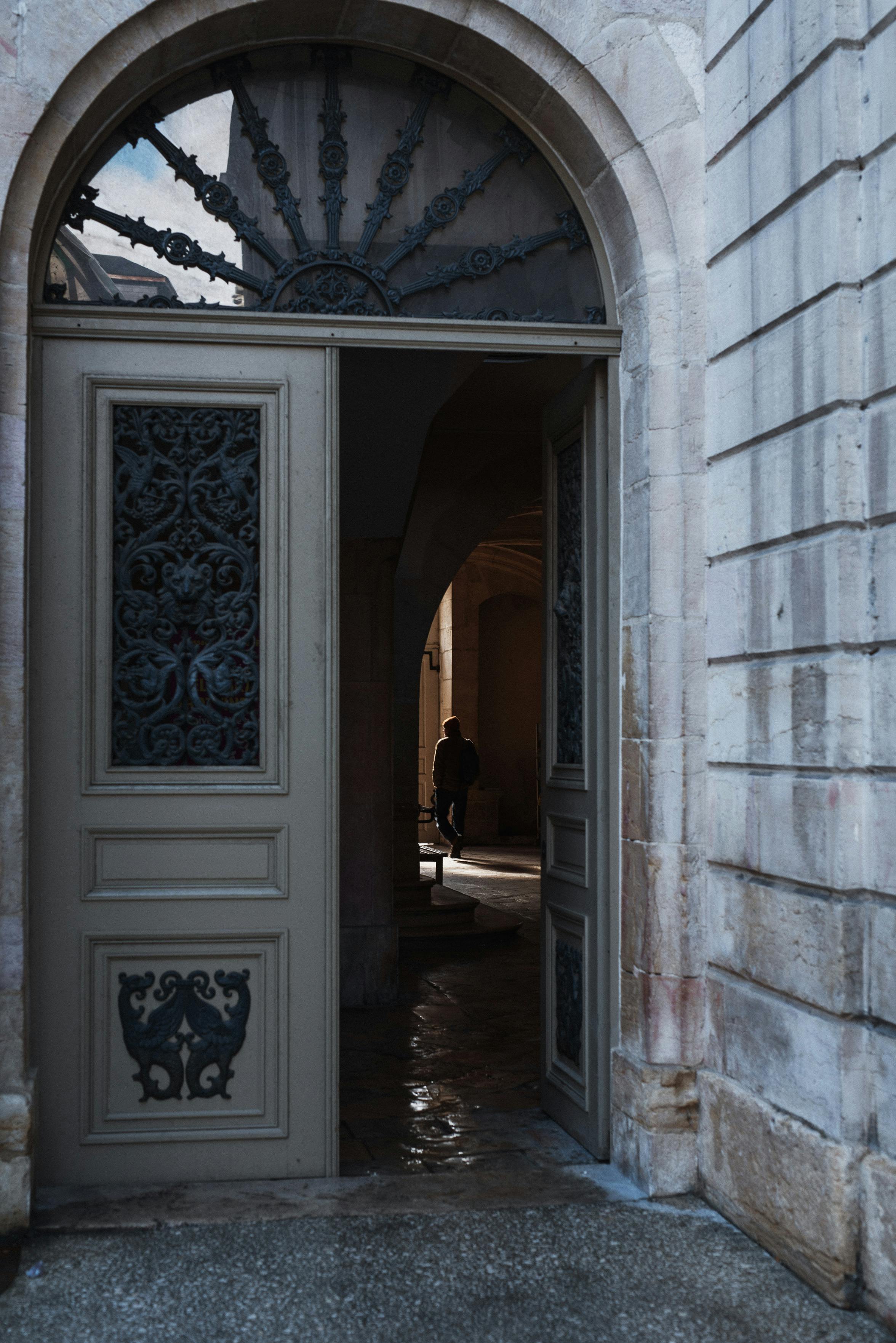 бесплатная Распахнутая богато украшенная дверь открывает вид на элегантный внутренний коридор с силуэтом в центре. Стоковое фото