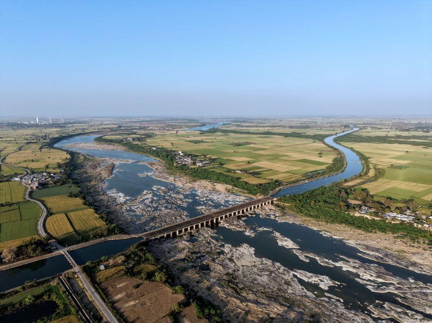 A stunning aerial shot of a river bridging lush green farmlands in India.