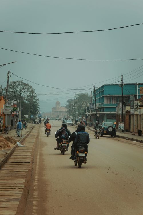 Free Motorcyclists travel along a dusty city road shrouded in fog, capturing urban life. Stock Photo