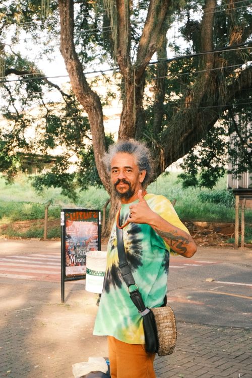 Free Man in tie-dye shirt gives thumbs up in a sunny Piracicaba park setting. Stock Photo