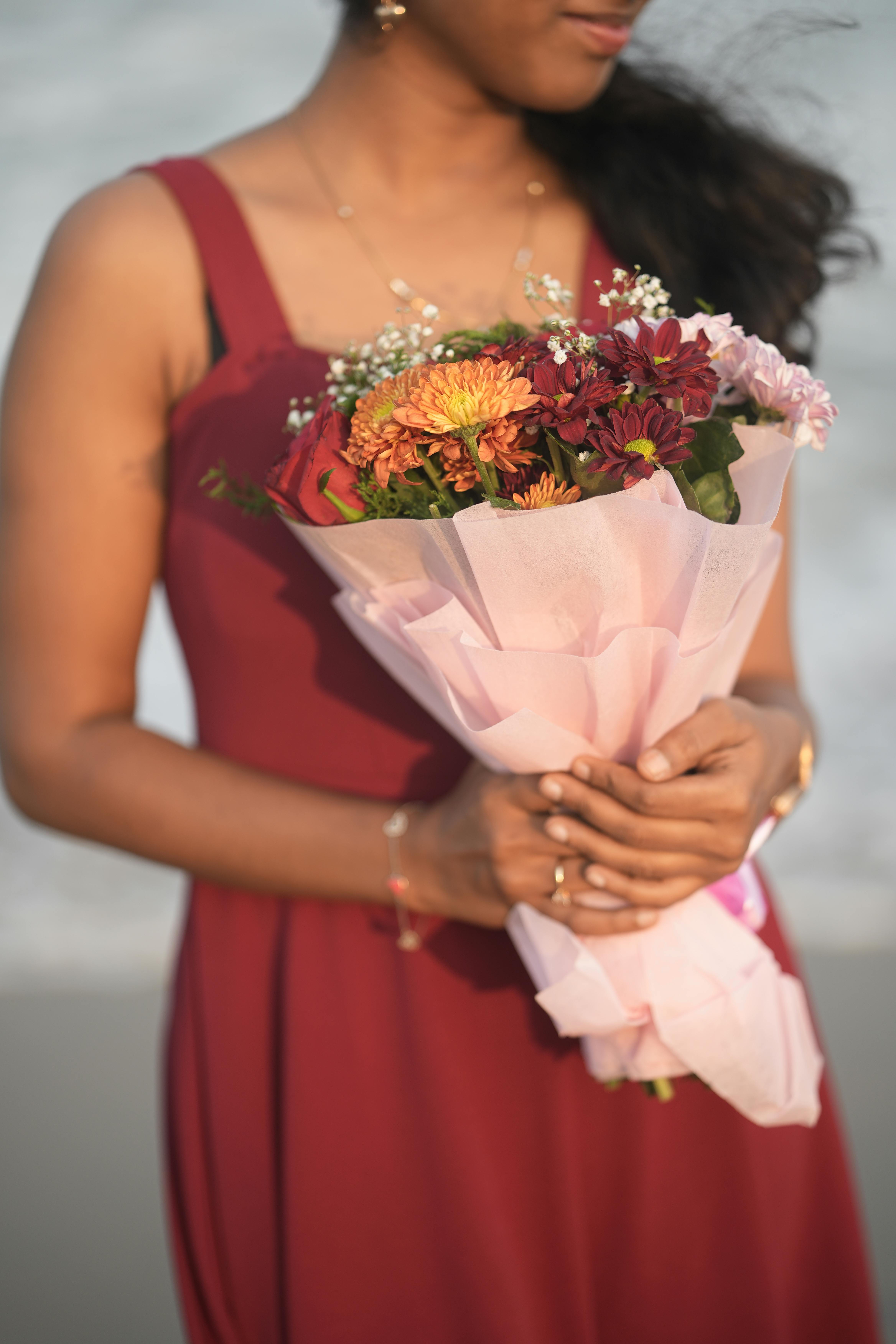 無料 晴れた日に鮮やかな花束を持った赤いドレスを着た女性のクローズアップ。 写真素材