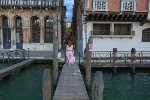 Free Woman in floral dress walking along a wooden dock beside a Venetian canal. Stock Photo
