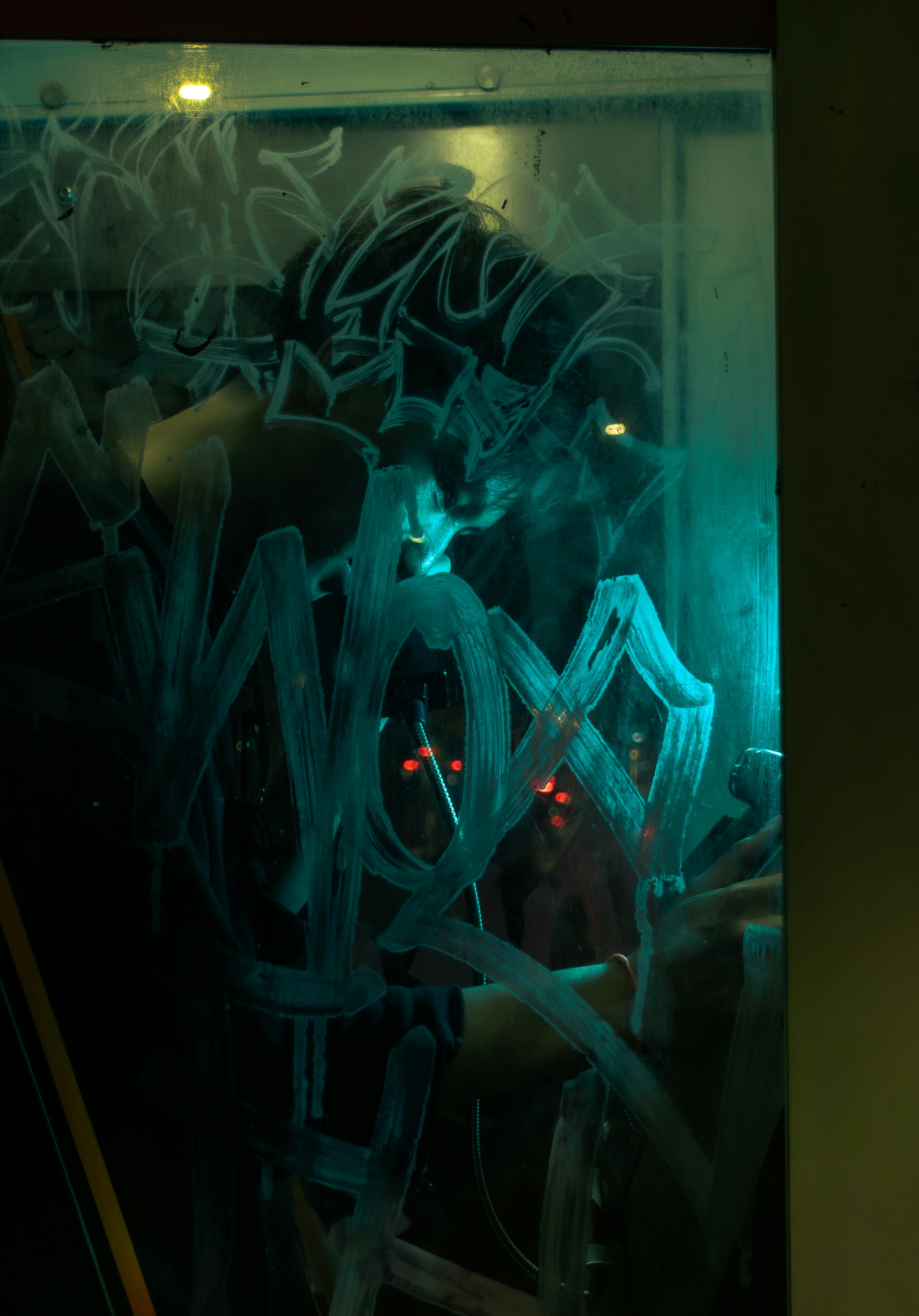 Gratis Una persona escribe en una ventana empañada bajo una iluminación tenue y artística, creando una atmósfera misteriosa. Foto de stock