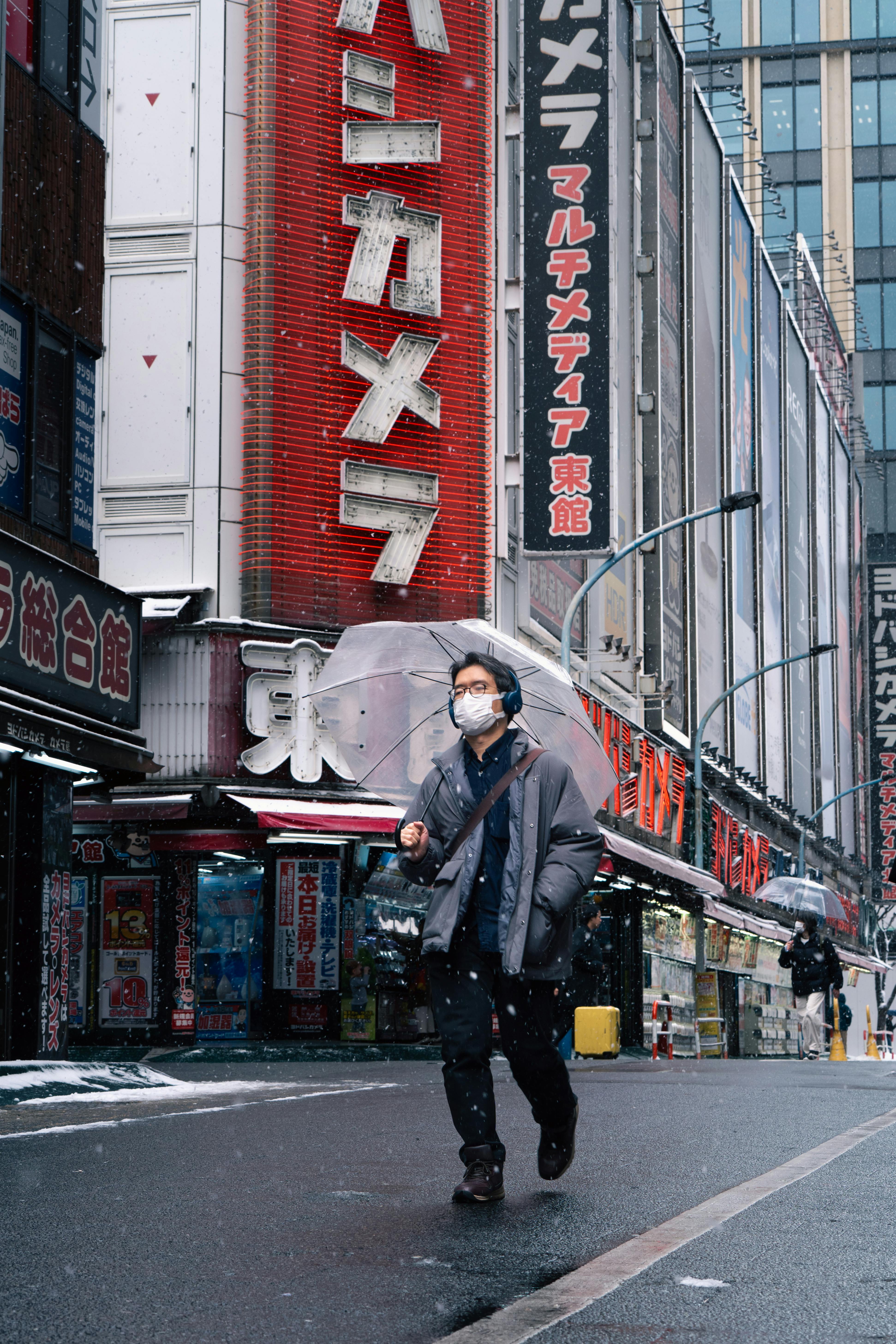 бесплатная Мужчина с зонтом идет по токийской улице с яркими вывесками магазинов. Стоковое фото