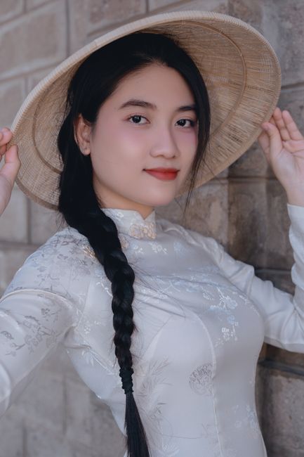 Close-up portrait of an adult woman in traditional Vietnamese dress with a bamboo hat.