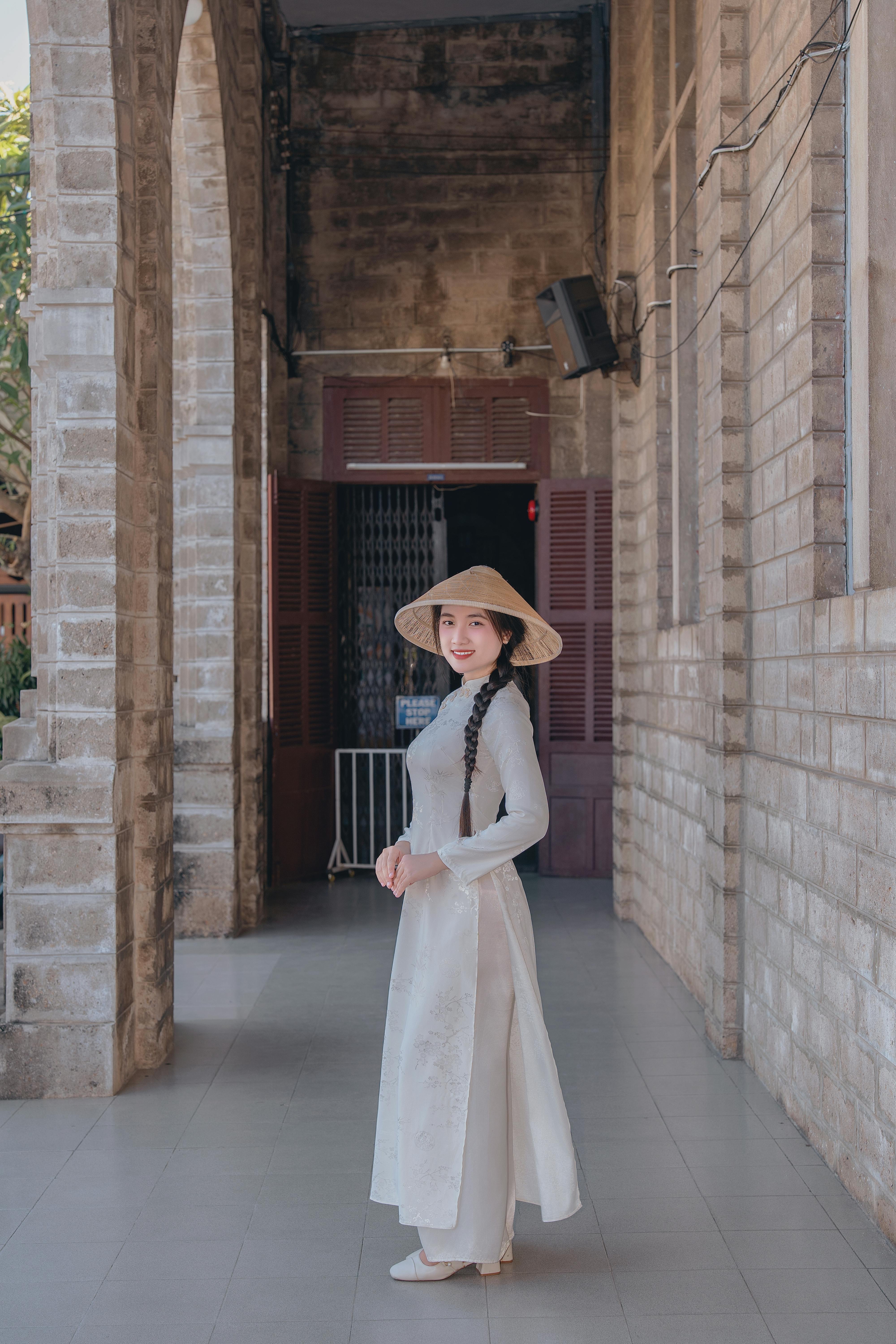 бесплатная Элегантная женщина в белом платье ао дай и конической шляпе в историческом здании. Стоковое фото