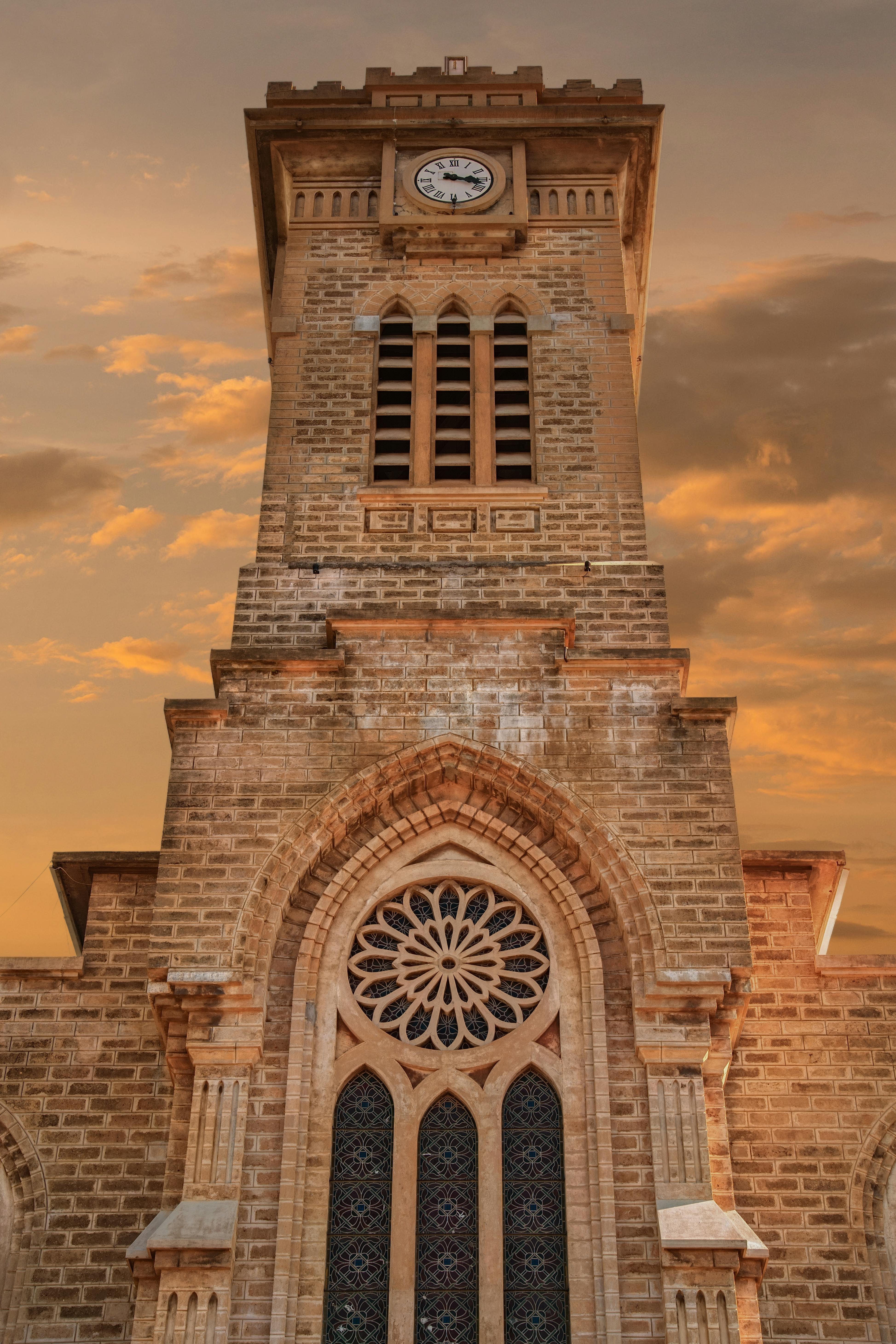 無料 ドラマチックな夕焼け空を背景に、精巧な建築ディテールが特徴的な美しい歴史ある時計塔がそびえ立っています。 写真素材