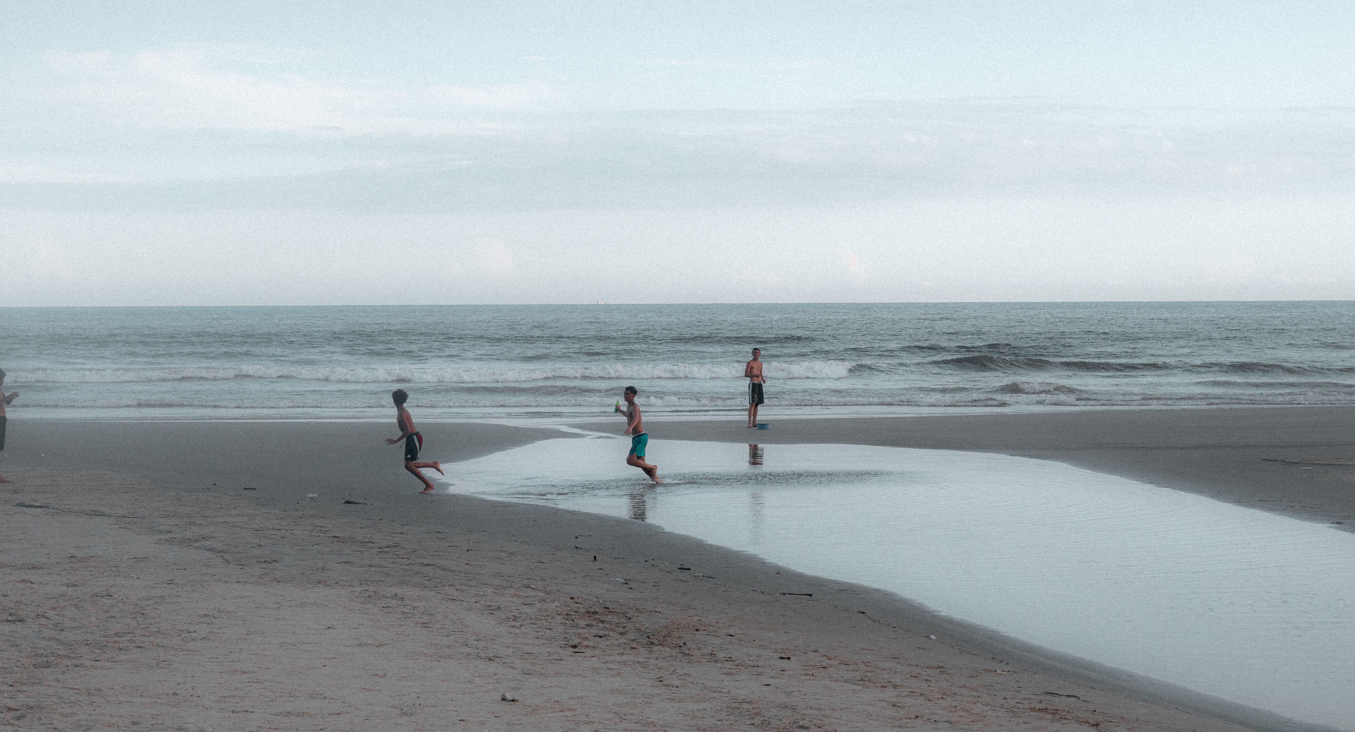 ฟรี เด็กสามคนกำลังสนุกสนานอยู่ที่ชายหาดอันเงียบสงบแห่งหนึ่ง คลังภาพถ่าย
