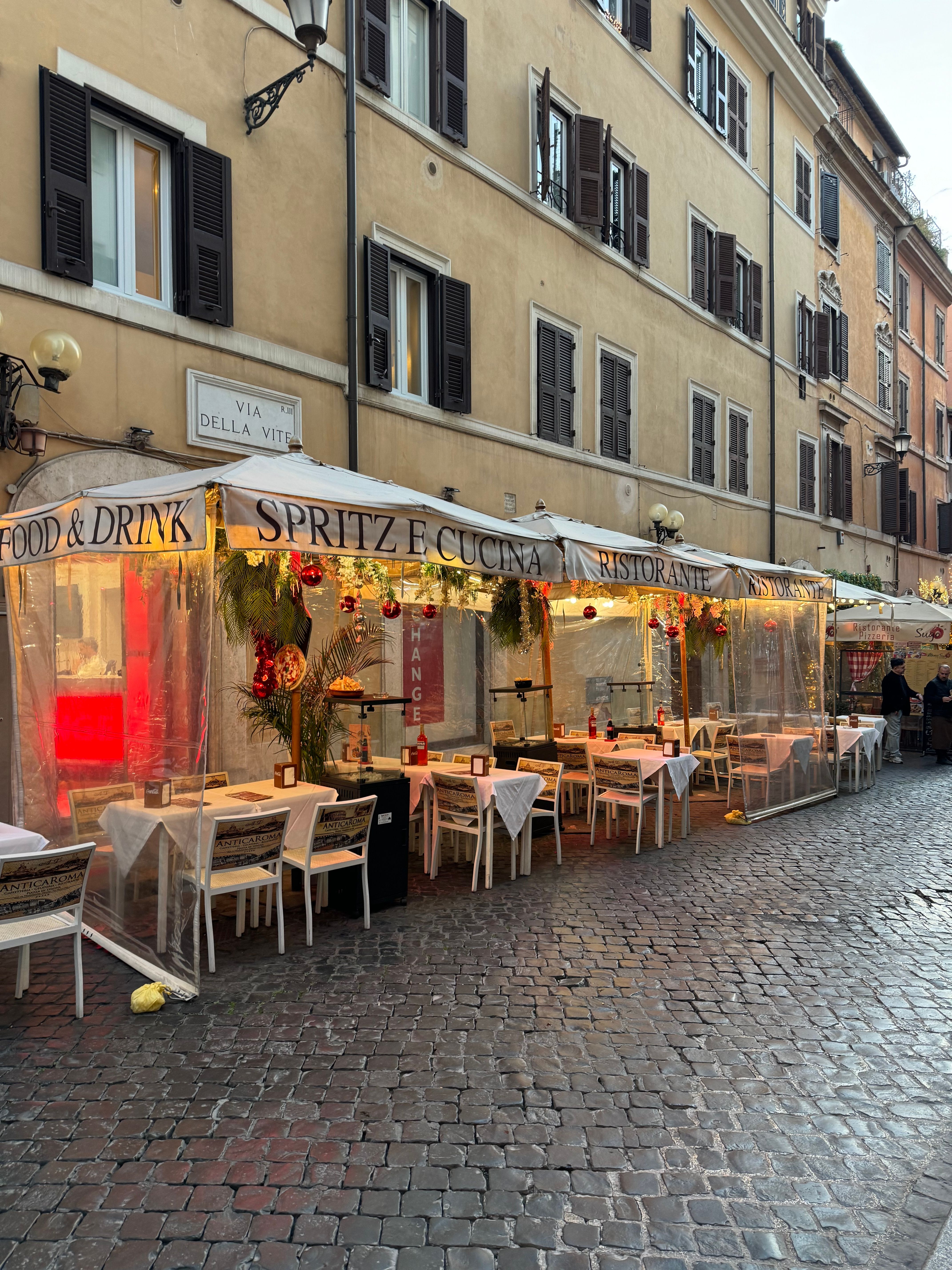 A cozy street-side cafe with al fresco dining in Rome, highlighting its charming architectural surroundings.