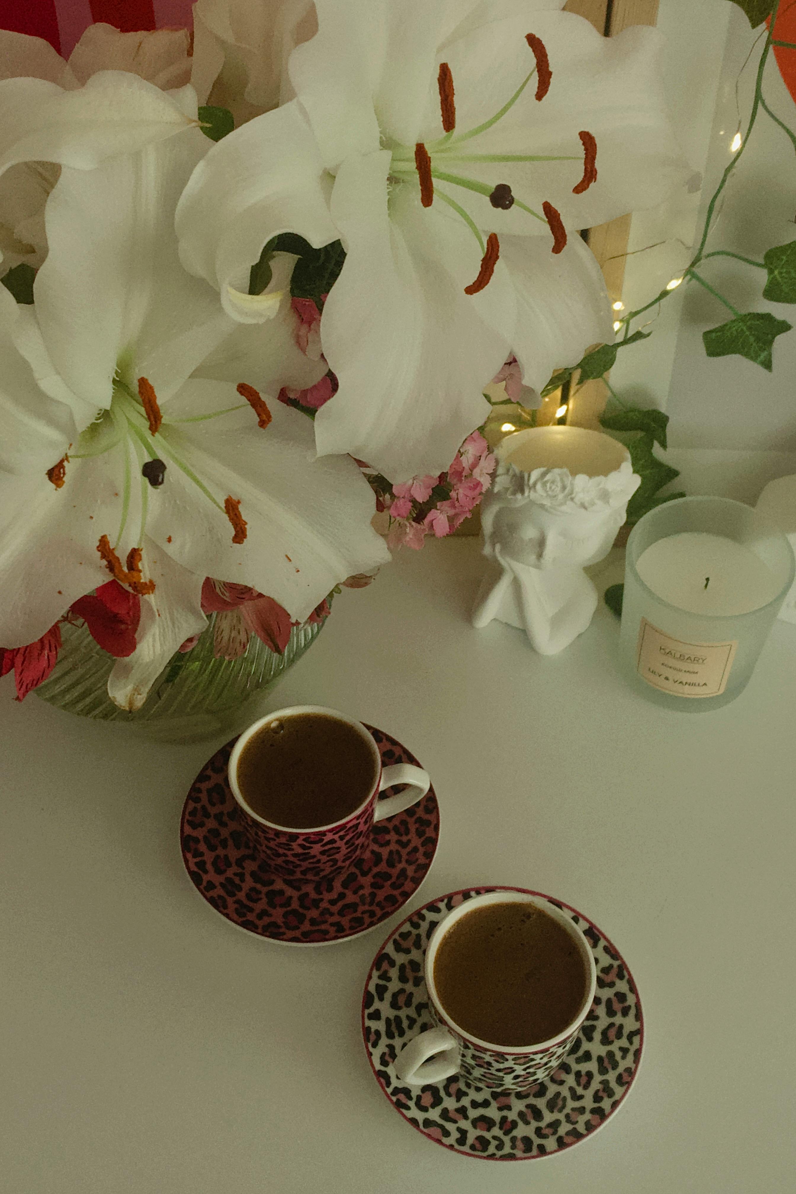 無料 テーブルの上に白いユリ、2 つのカップ、香りのよいキャンドルが置かれたエレガントなコーヒーシーン。 写真素材