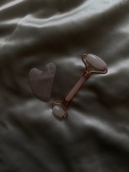 A rose quartz facial roller and gua sha tool rest on soft silk, embodying luxury skincare.