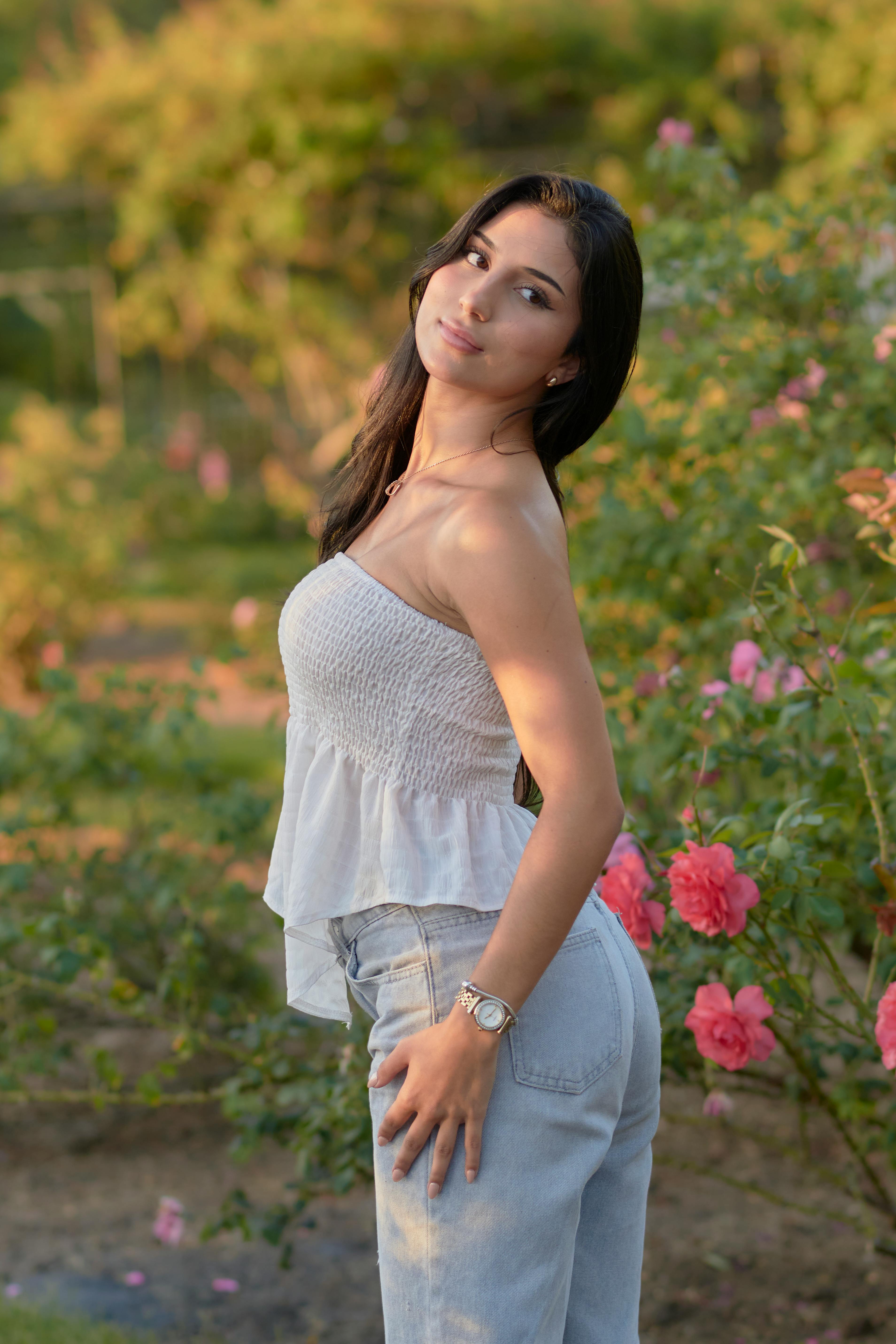 Free Portrait of a young woman in a sunny rose garden, capturing a serene and warm atmosphere. Stock Photo
