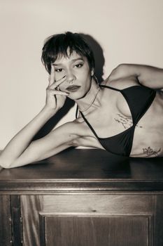 Stylish monochrome portrait of a woman with tattoos in a black bikini top posing thoughtfully.