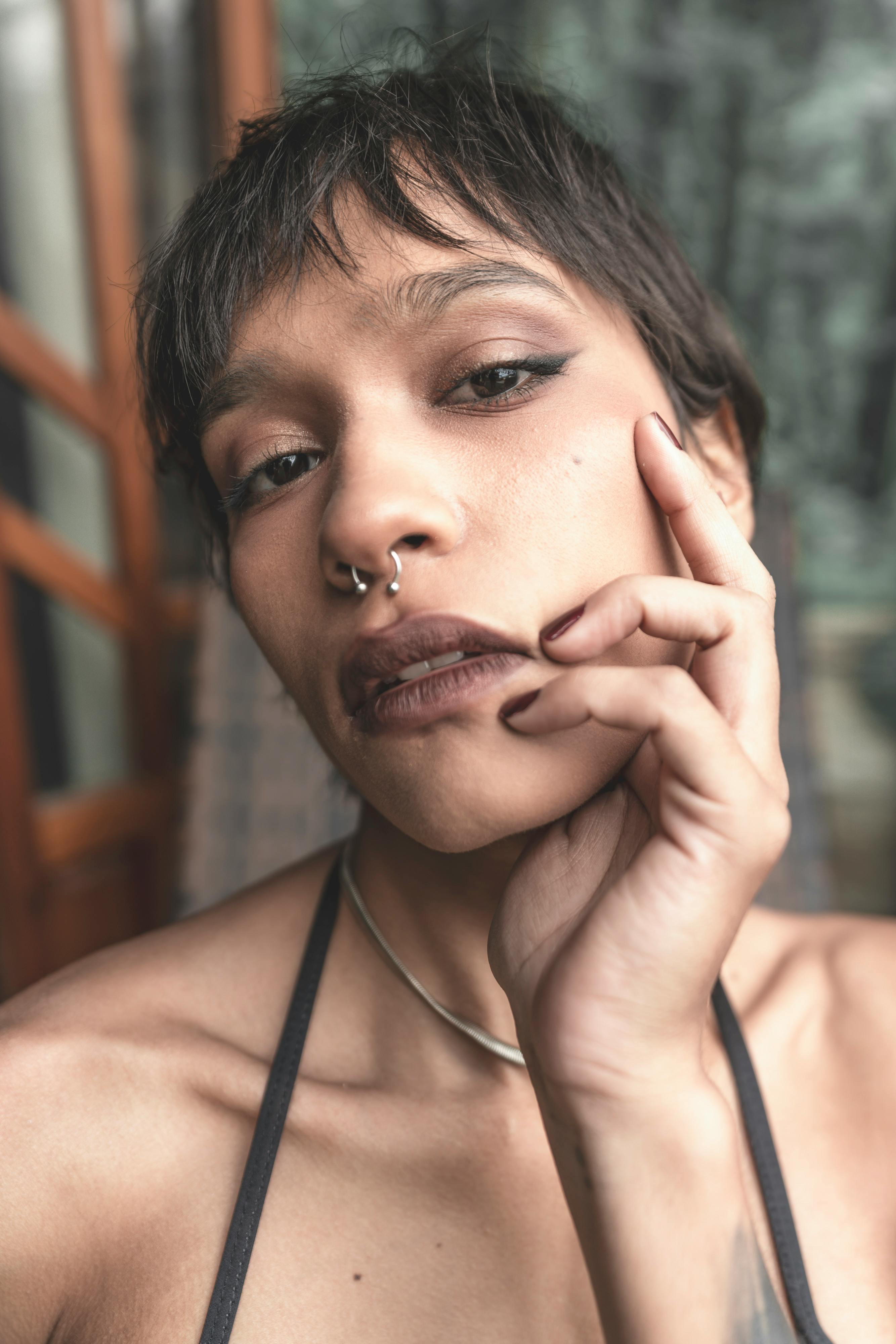 Gratis Gambar close-up seorang wanita muda dengan tindik hidung, riasan minimal, dan ekspresi termenung. Foto Stok