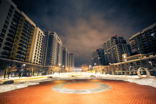 City night scene featuring tall residential buildings with a plaza, captured in winter.