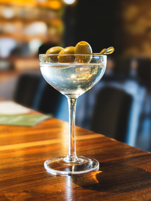 A dry martini in a chilled coupe glass with three green olives on a cocktail pick, condensation beading on the glass