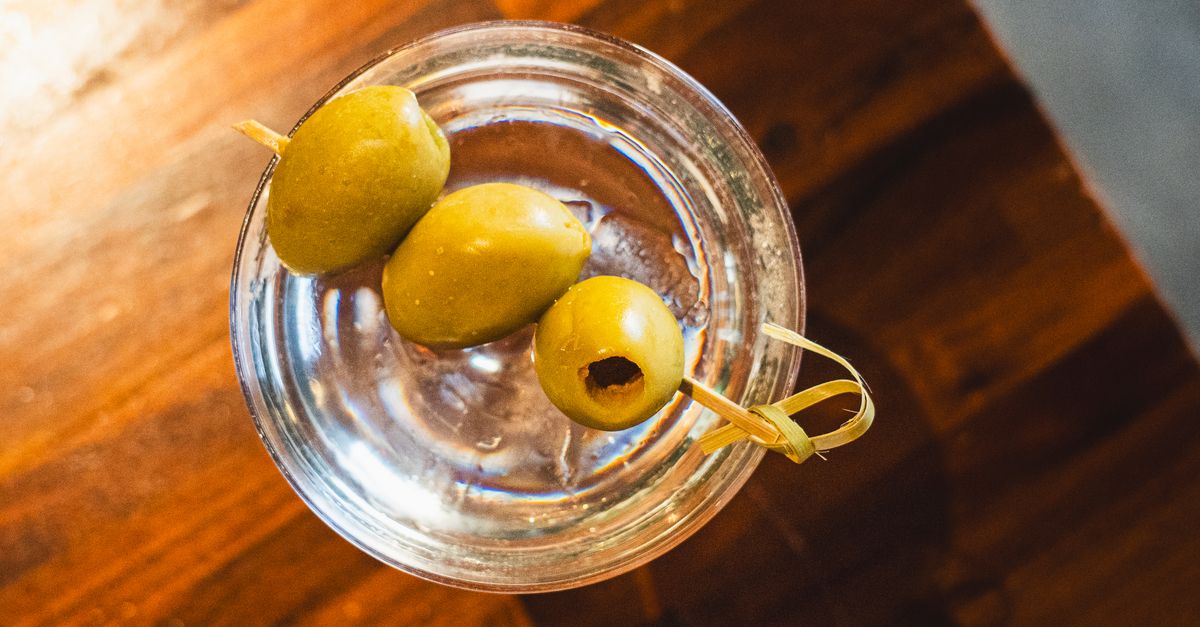 Top view of a classic martini cocktail garnished with green olives in a glass.
