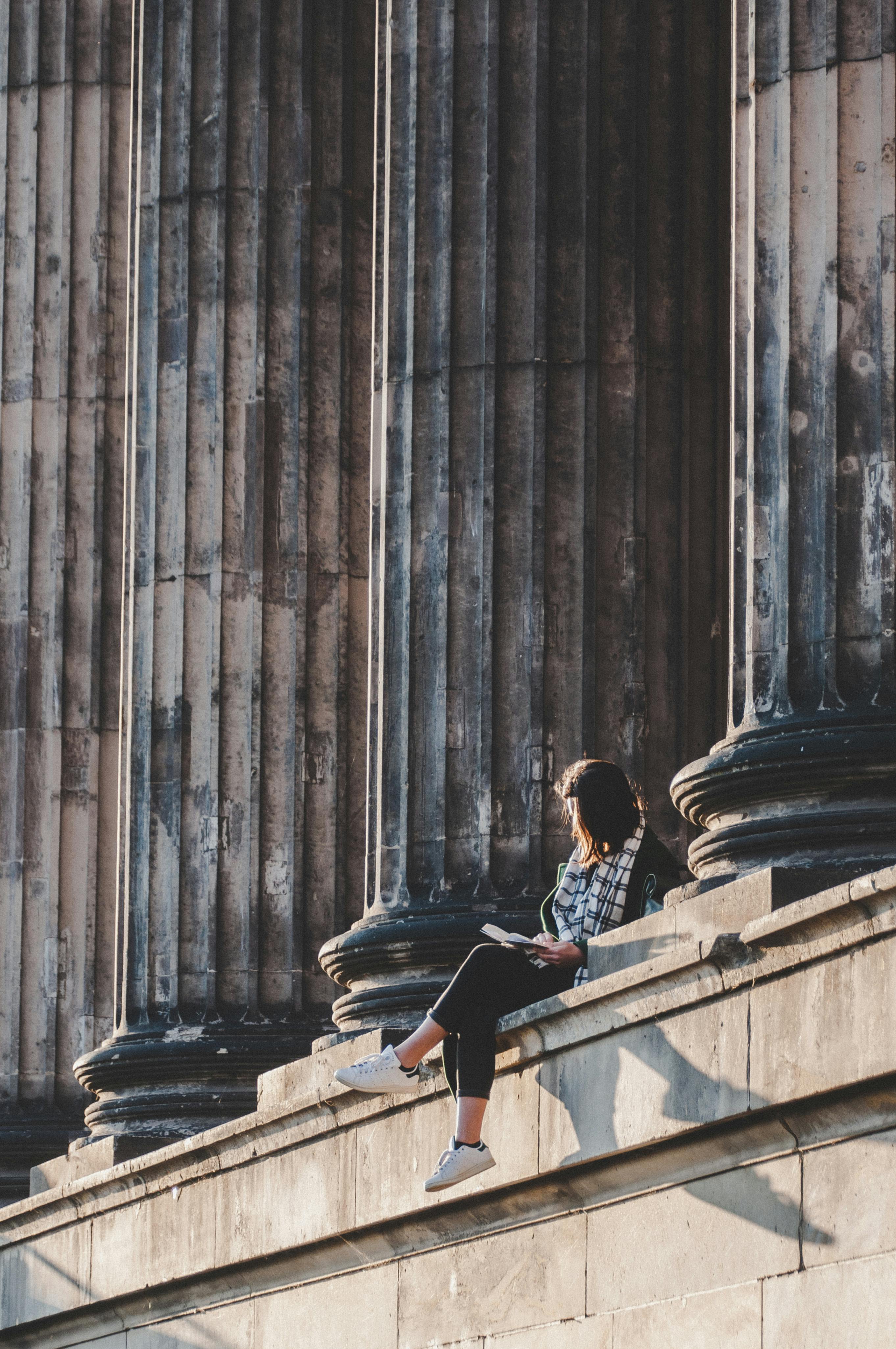 gratis Een vrouw zit in alle rust te lezen, omringd door imposante architectonische zuilen, en geniet van een moment van bezinning. Stockfoto