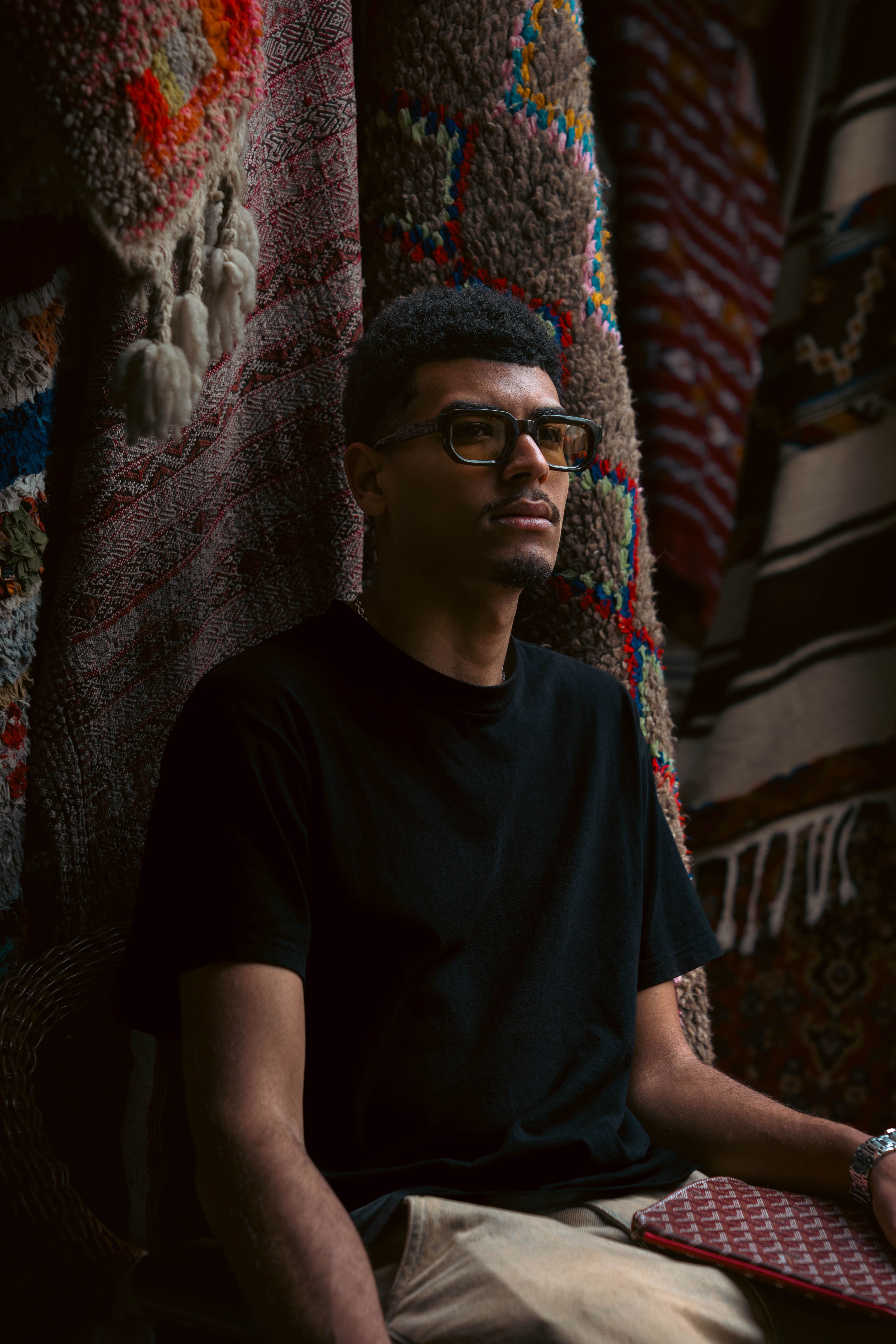 A man sits thoughtfully amidst vibrant Moroccan textiles in Casablanca.