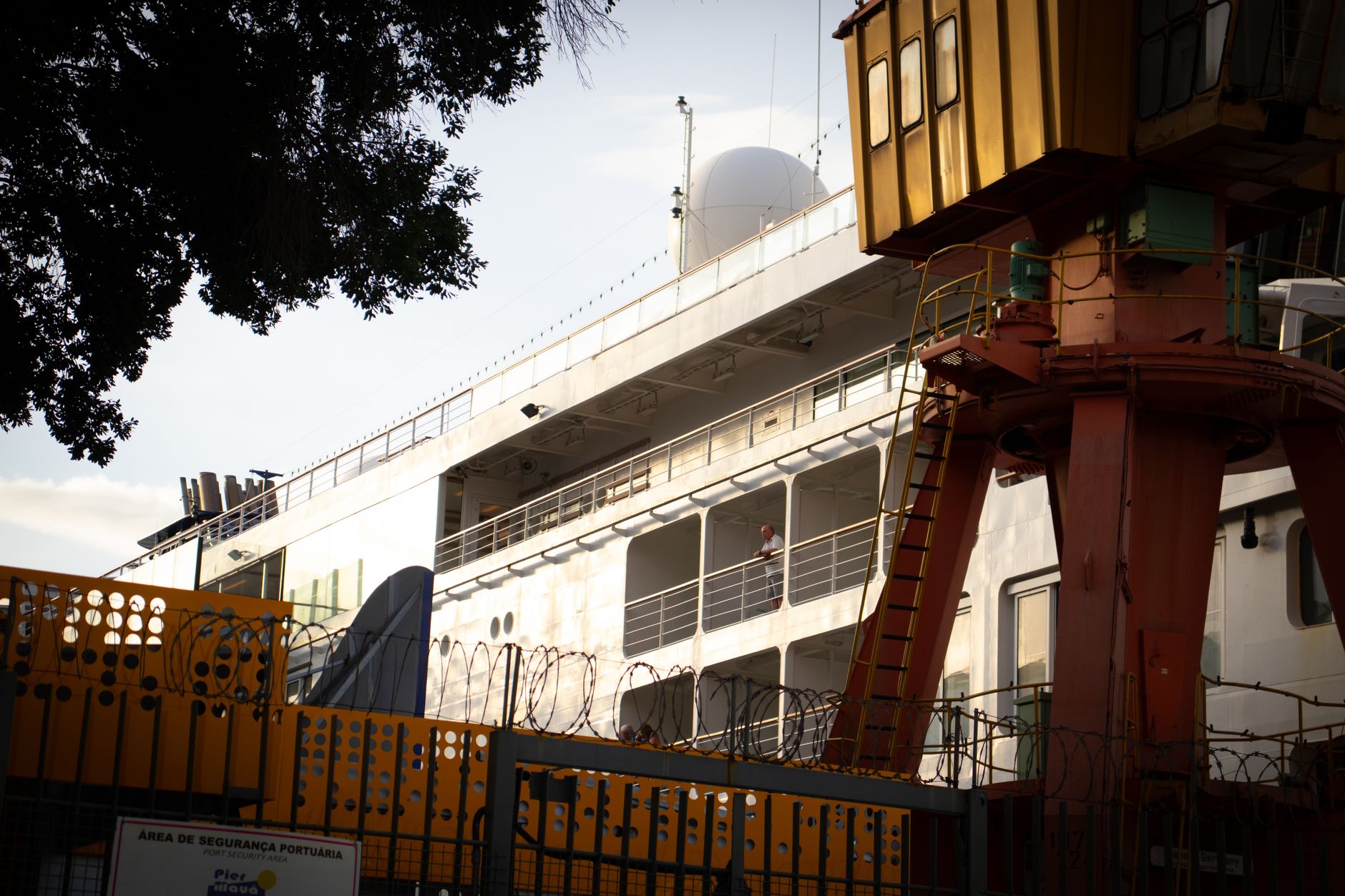 A cruise ship docked at Rio's port with security fencing and industrial crane in view.