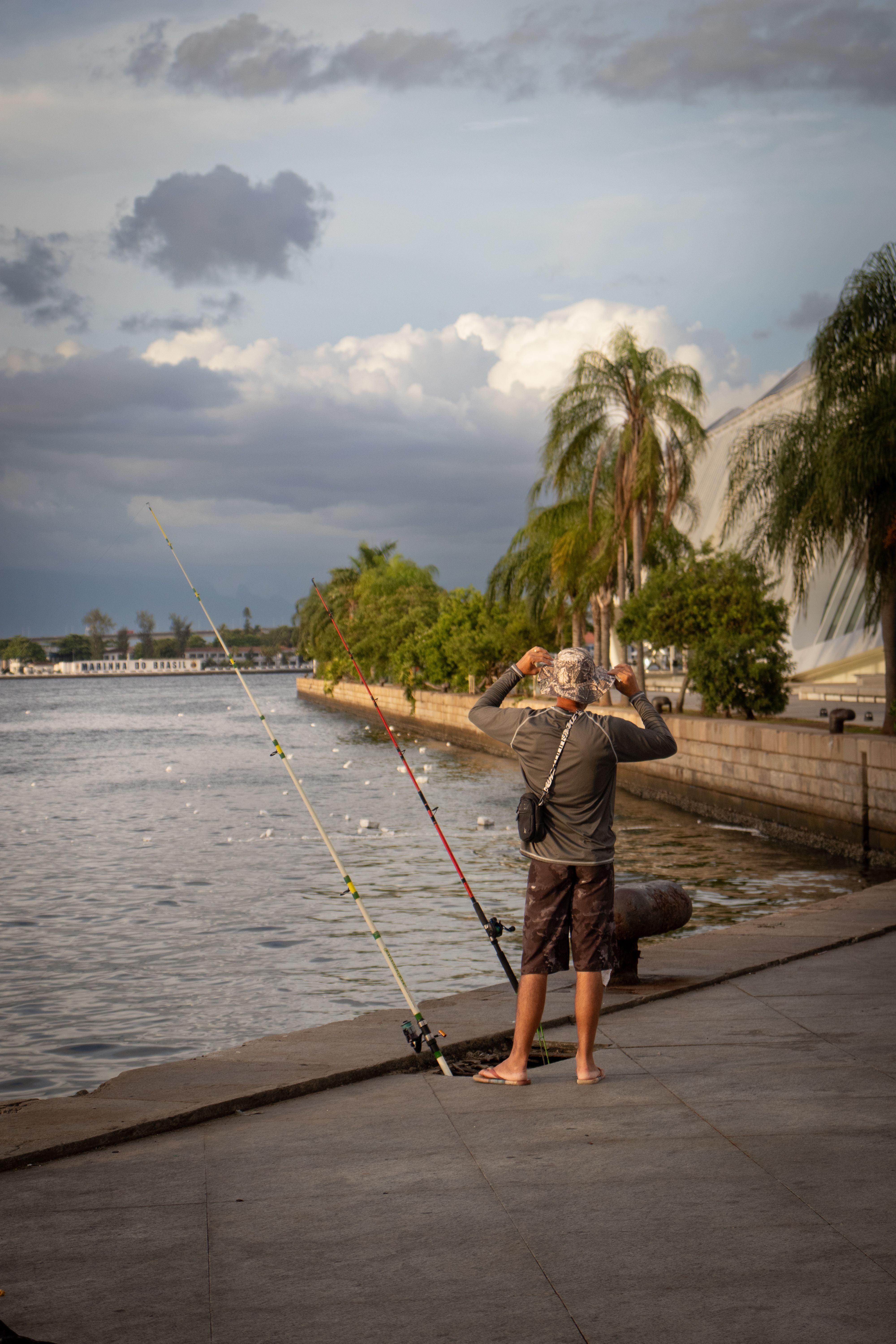 An adult man fishing by the Rio de Janeiro waterfront, cloudy sky, relaxing and serene setting.