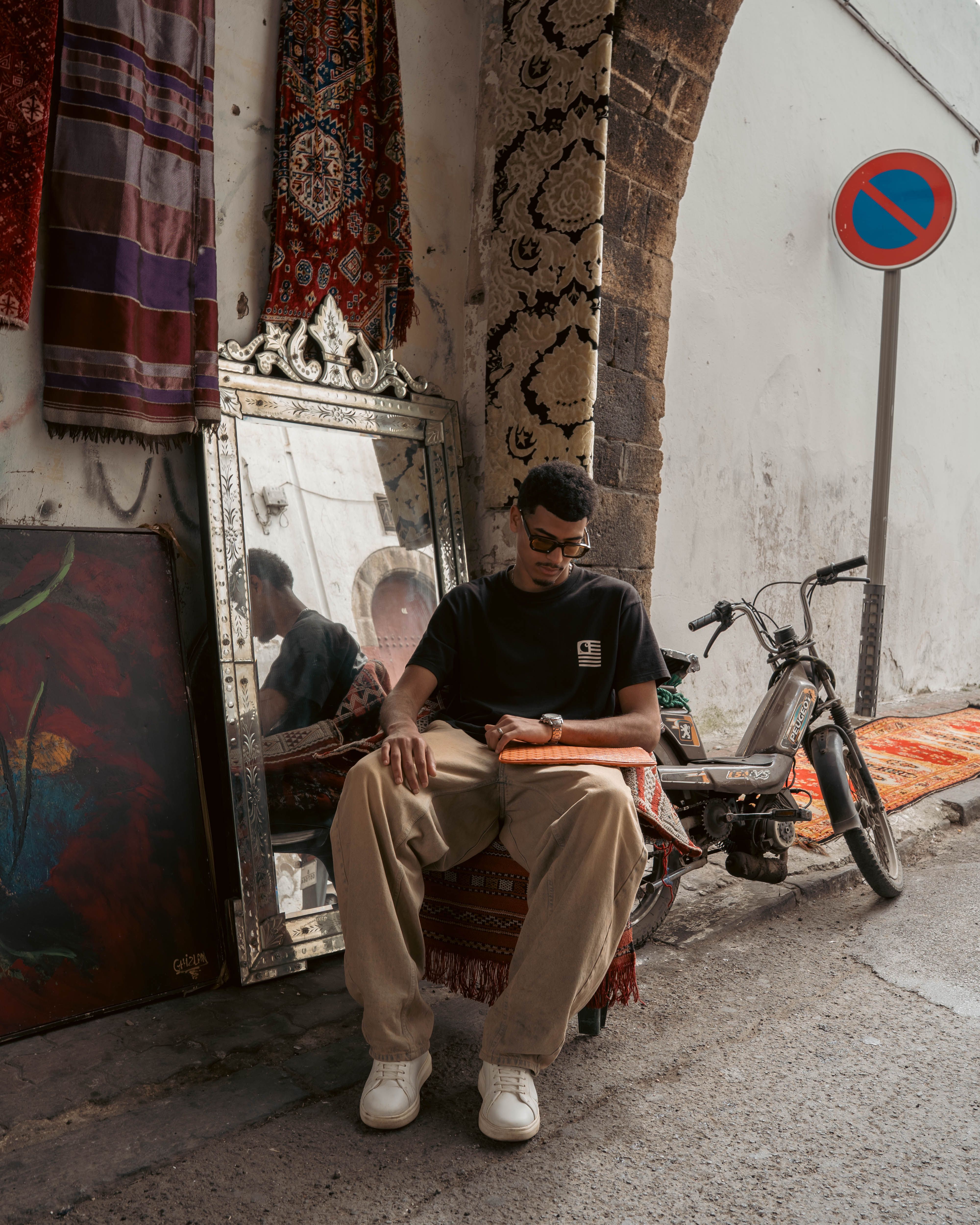A young artisan sitting outdoors in Casablanca with tapestries and a mirror, exuding local charm.