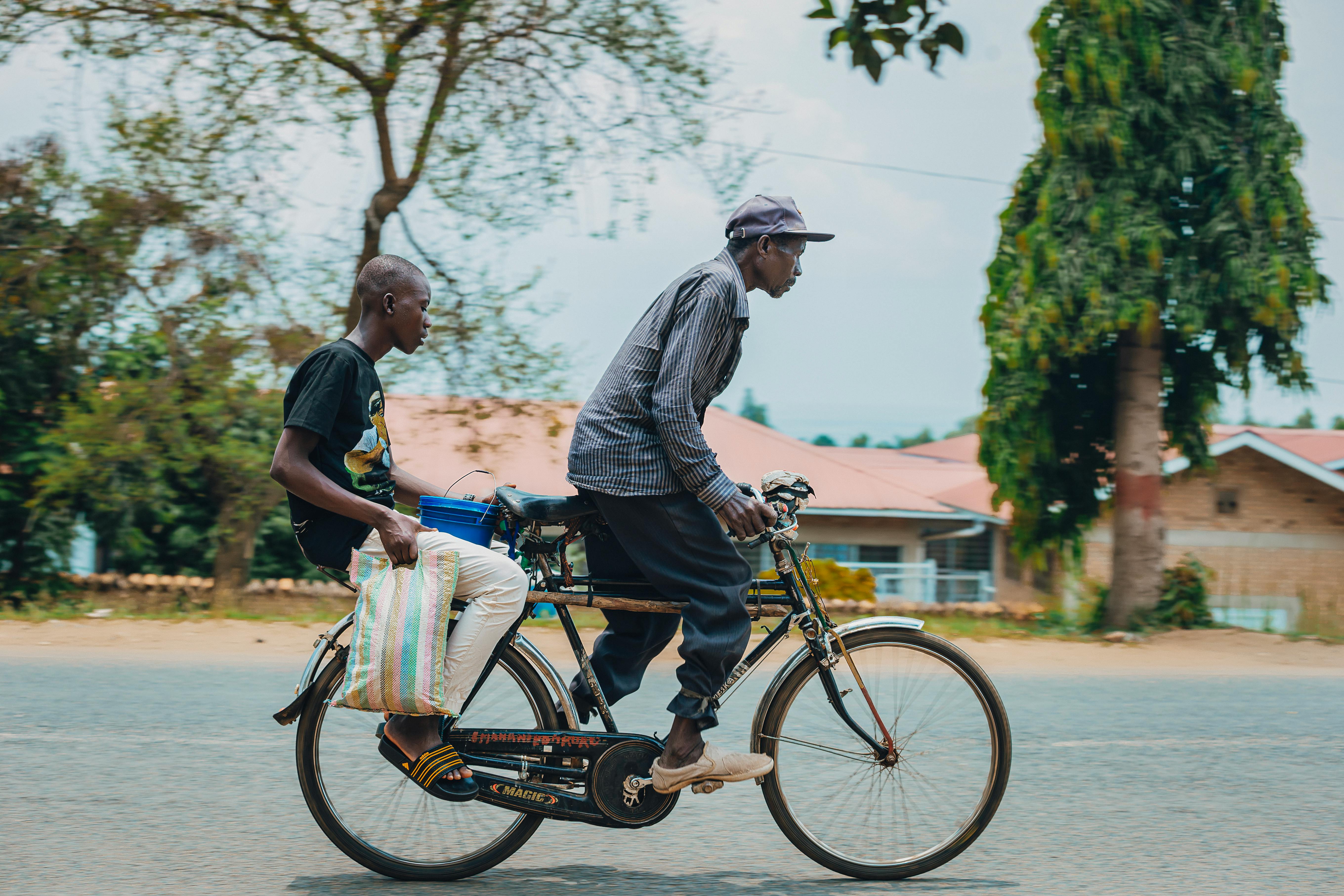 無料 晴れた日に木々や建物を背景に自転車に乗る男性 2 人。 写真素材