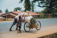 Child Helping Push Loaded Bicycle on Roadside