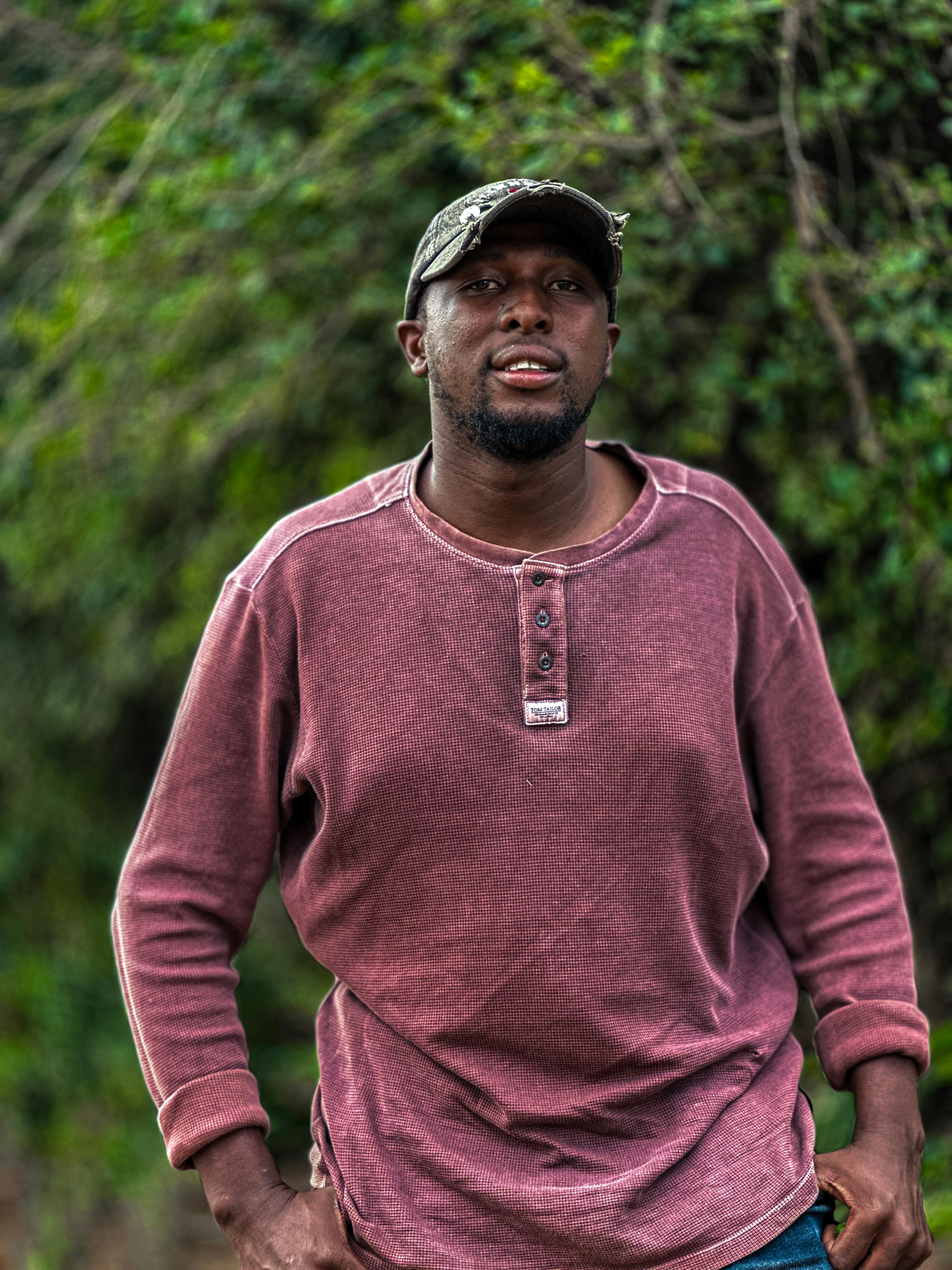 無料 帽子と長袖のシャツを着た男性が、緑の背景を背景に屋外でポーズをとっています。 写真素材