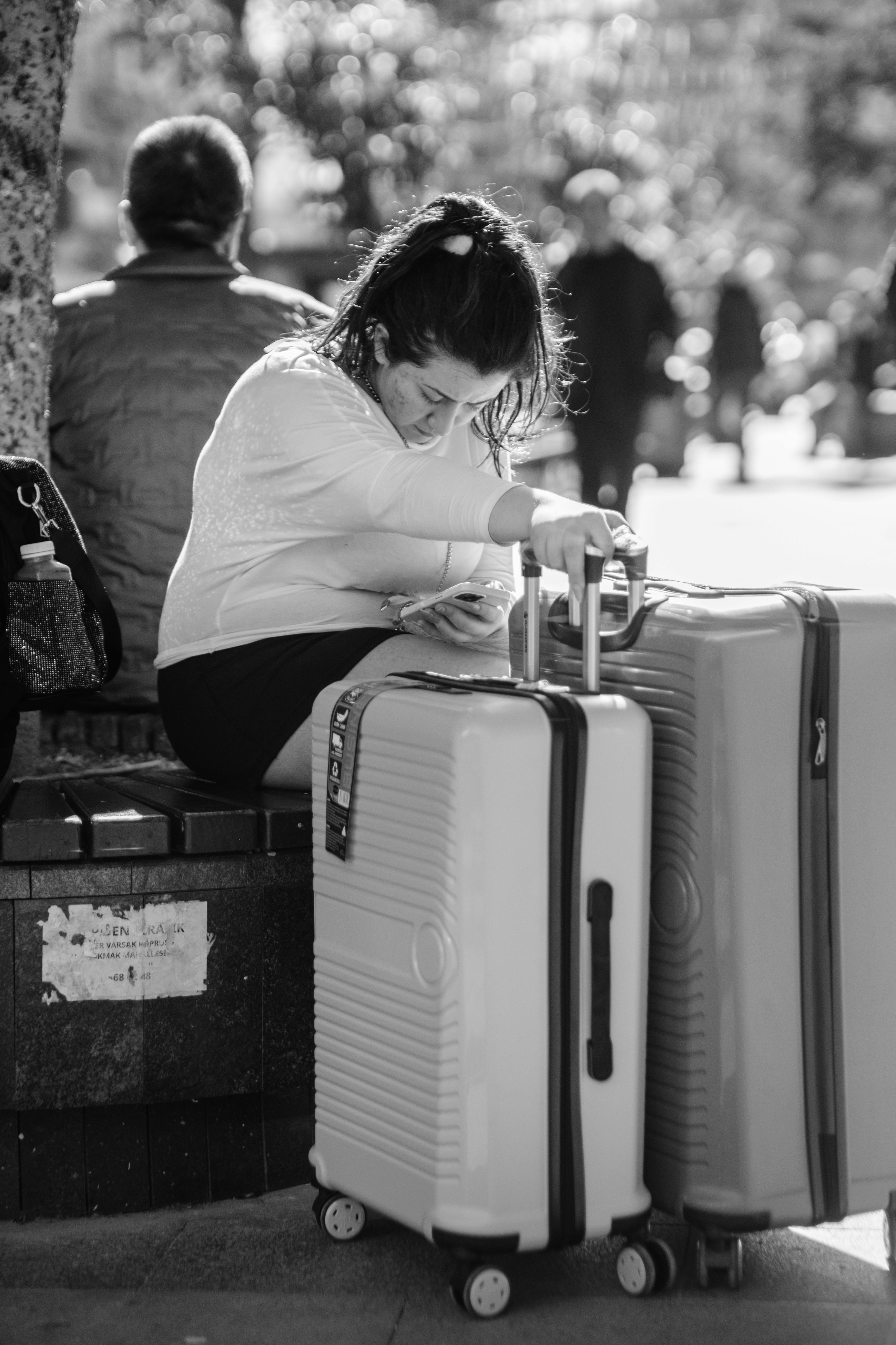 Kostnadsfria En kvinna sitter på ett torg med sina resväskor och förbereder sig för sin resa. Stock foto