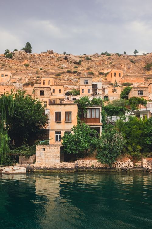 Free Charming historic homes perched on a cliff overlooking a peaceful lake under a cloudy sky. Stock Photo