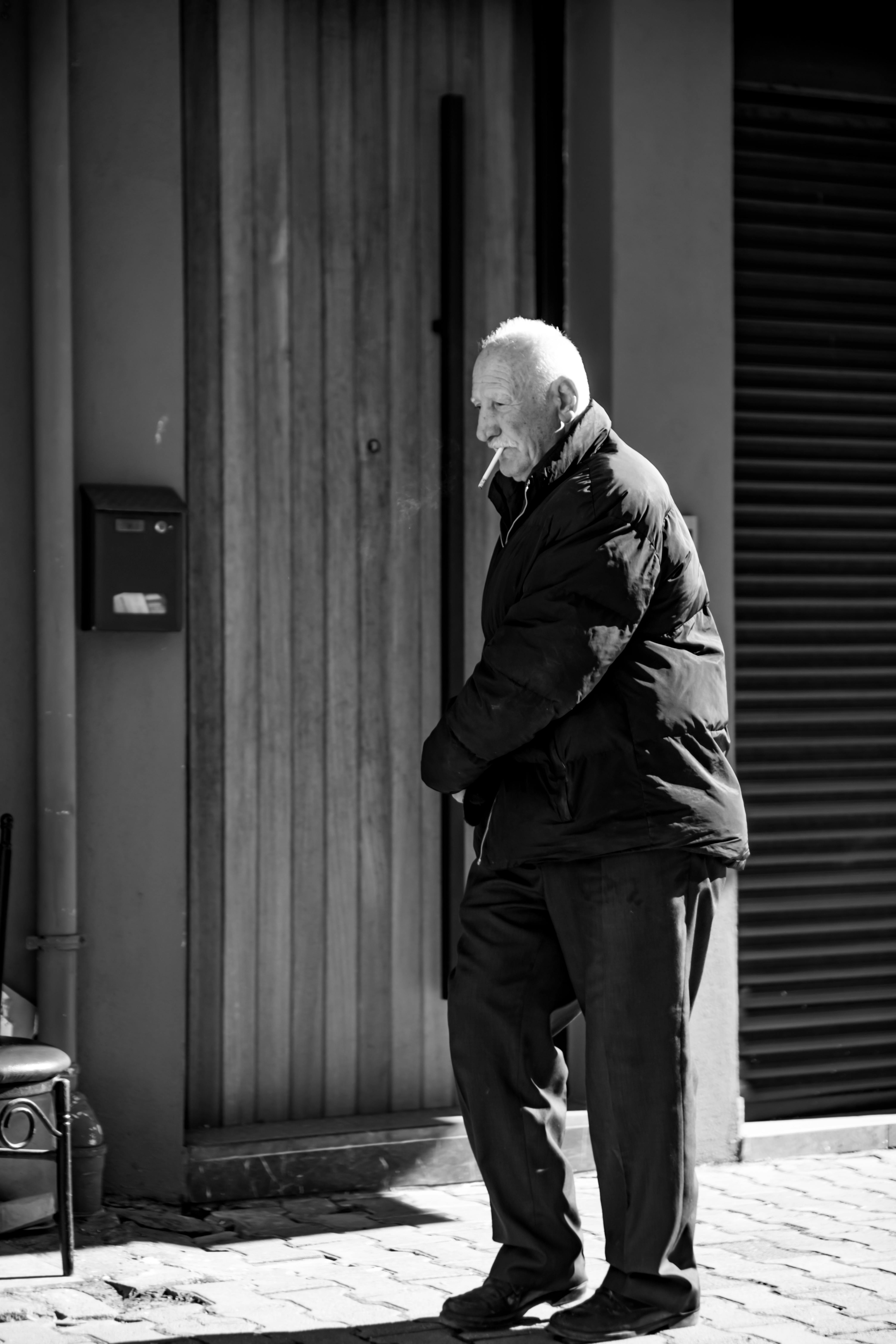 Free Black and white photo of an elderly man smoking in a city street environment. Stock Photo