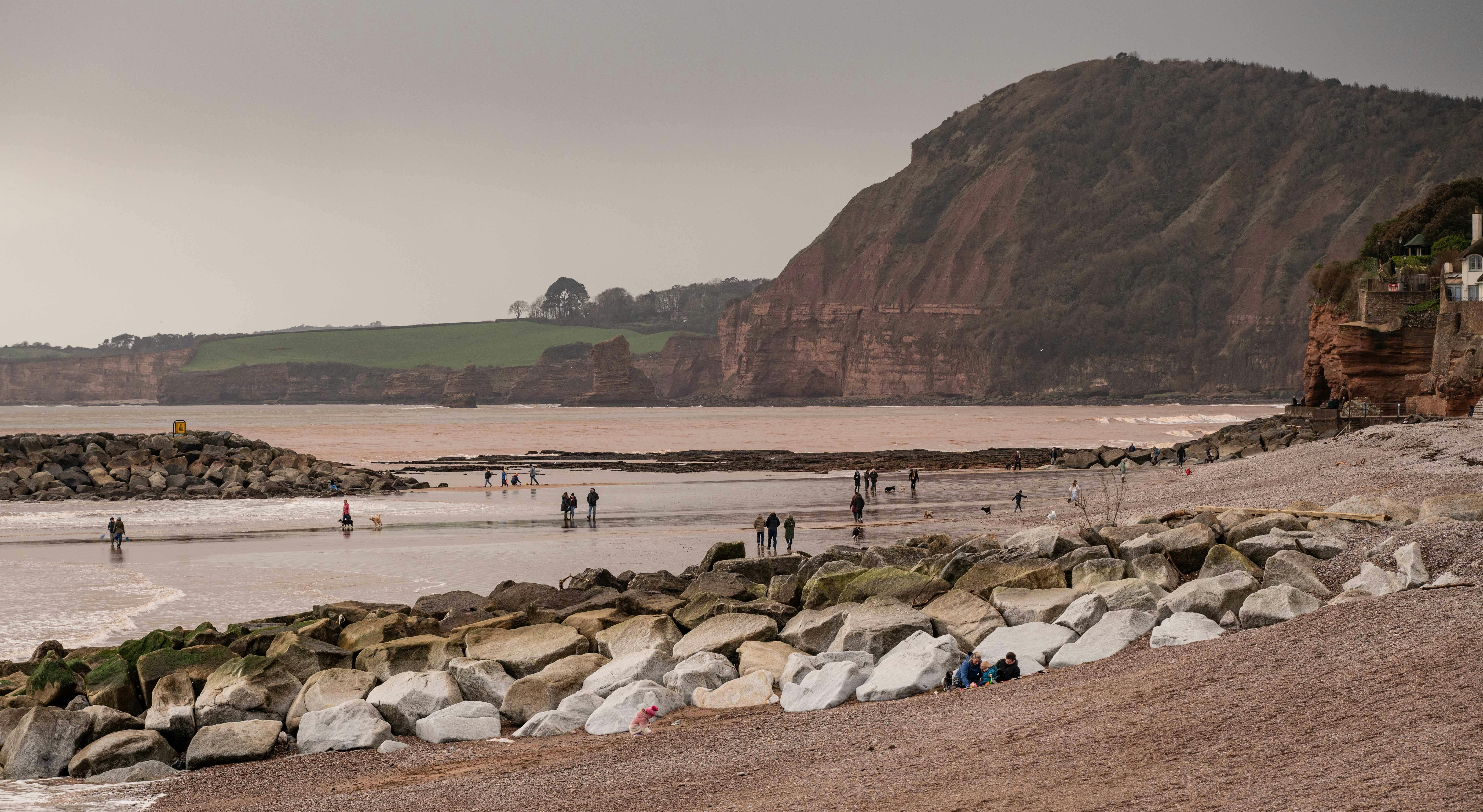 People strolling along a rocky beach at low tide with cliffs in the background.