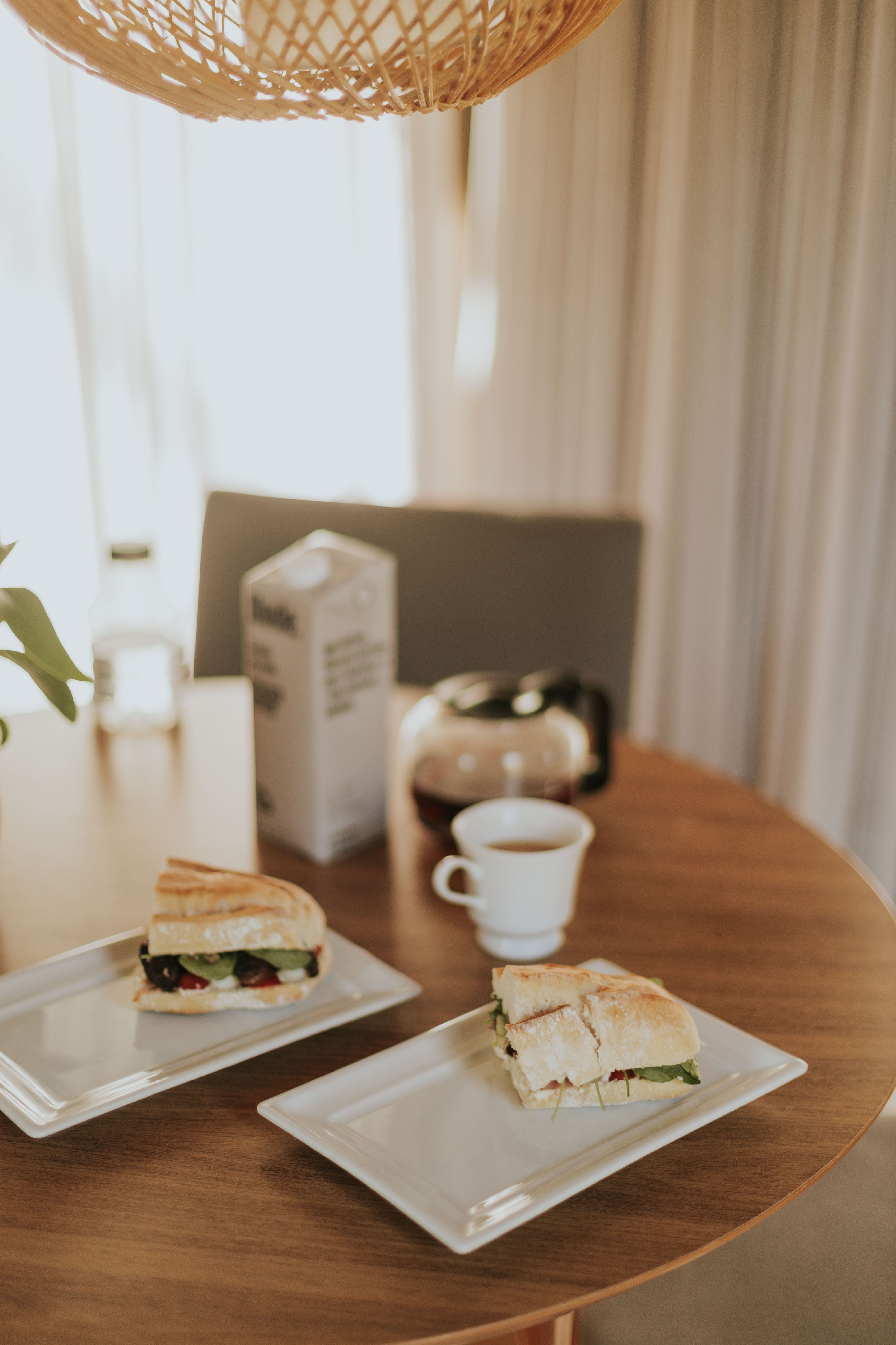 Cozy breakfast table with gourmet sandwiches and beverages in a sunlit dining room.