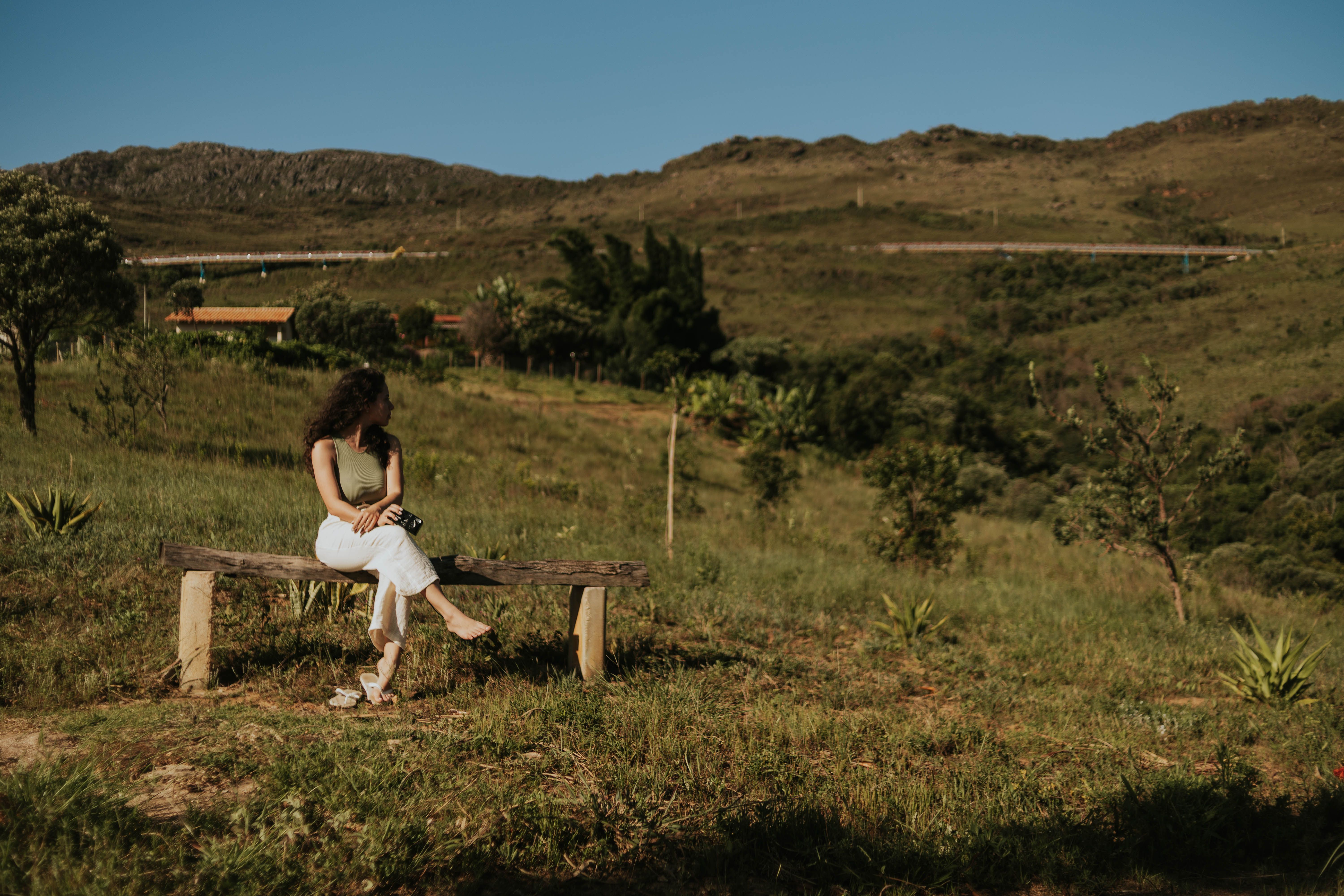 Woman sitting on a bench enjoying a lush grassy hillside under a clear blue sky.