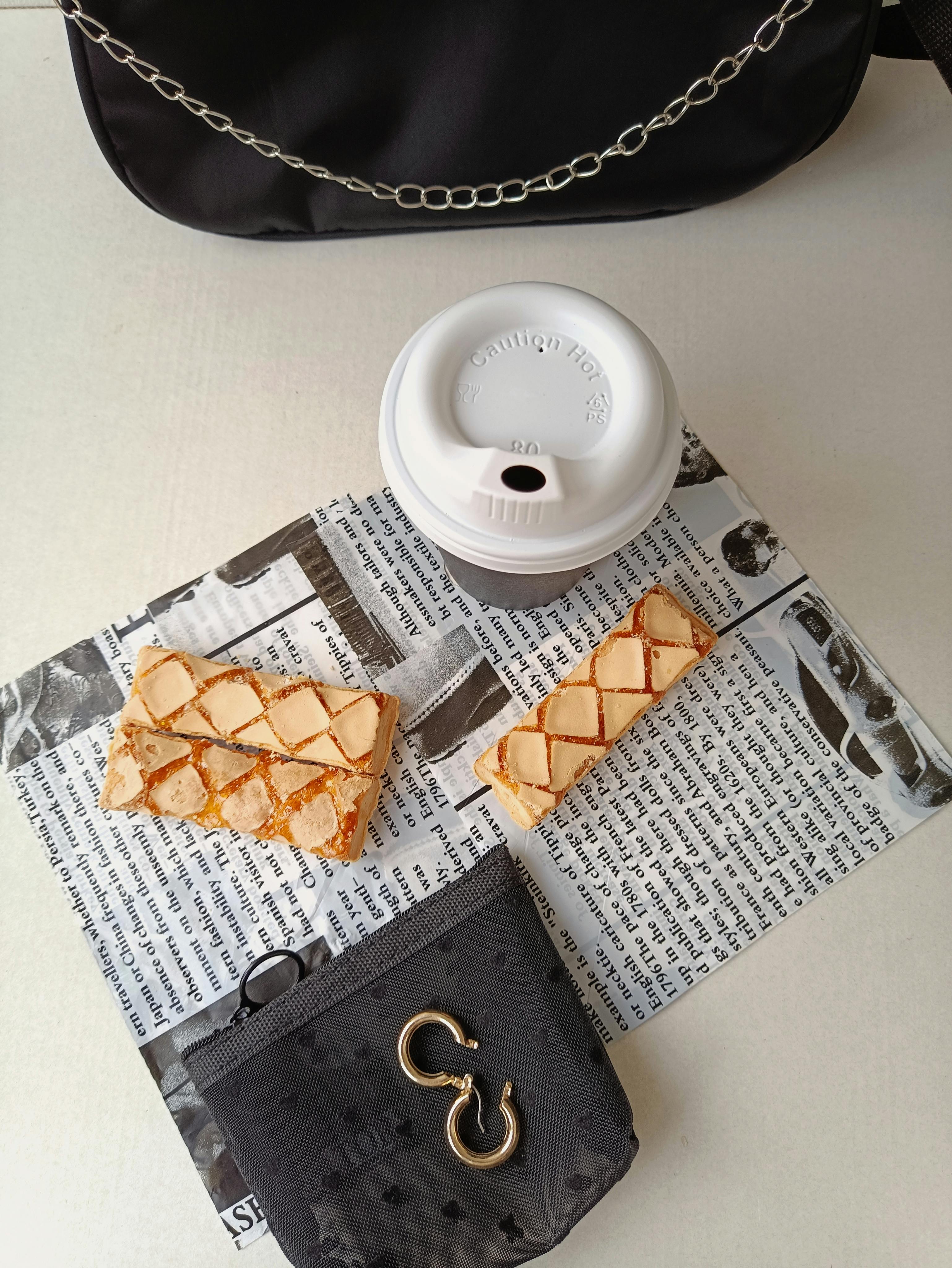 無料 朝の雰囲気にぴったりな、アクセサリー付きの新聞紙の上にコーヒーカップとビスコッティを平らに並べた画像です。 写真素材