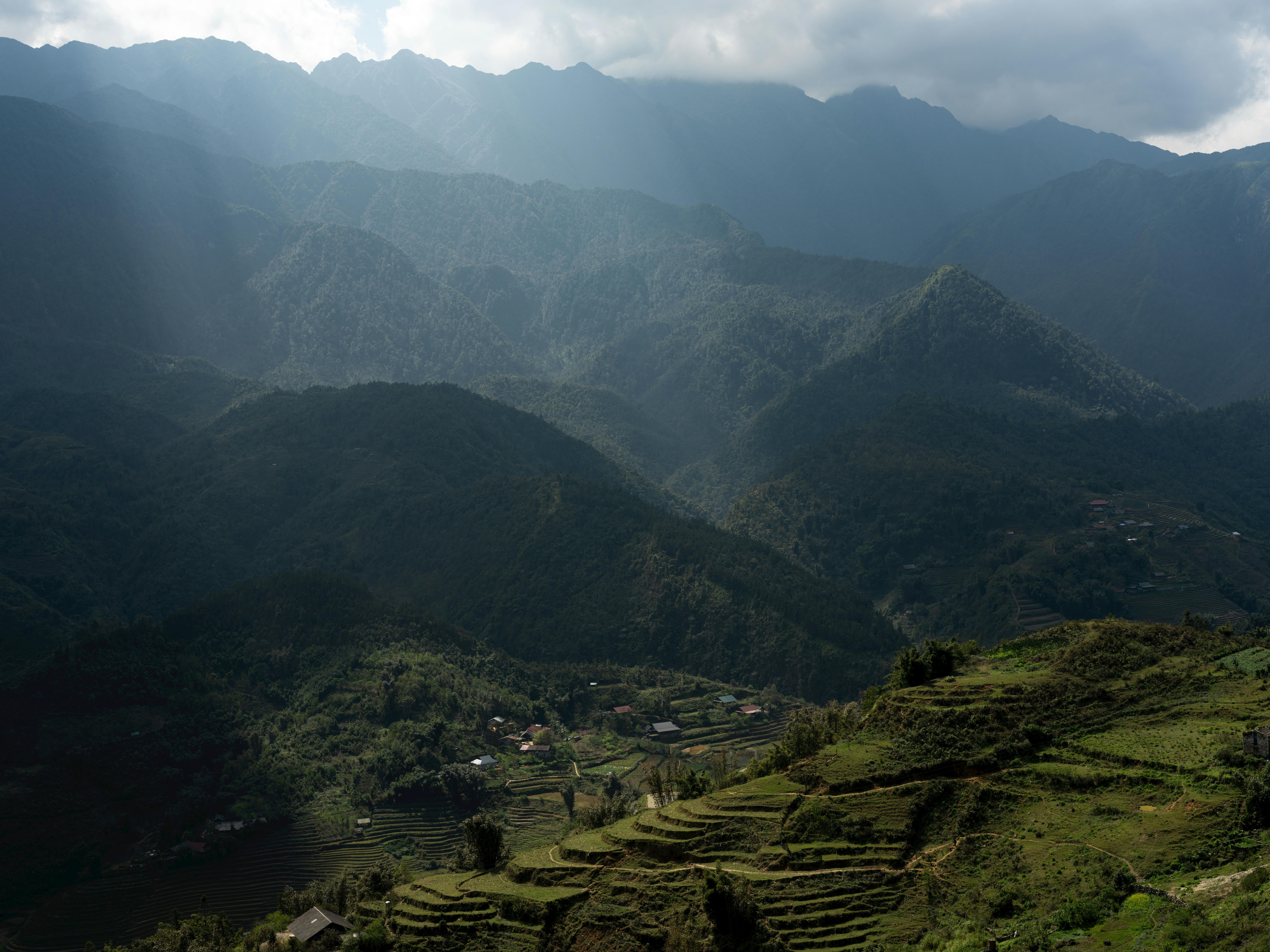 Majestic mountains and terraced fields under dramatic sky in Lào Cai, Vietnam.