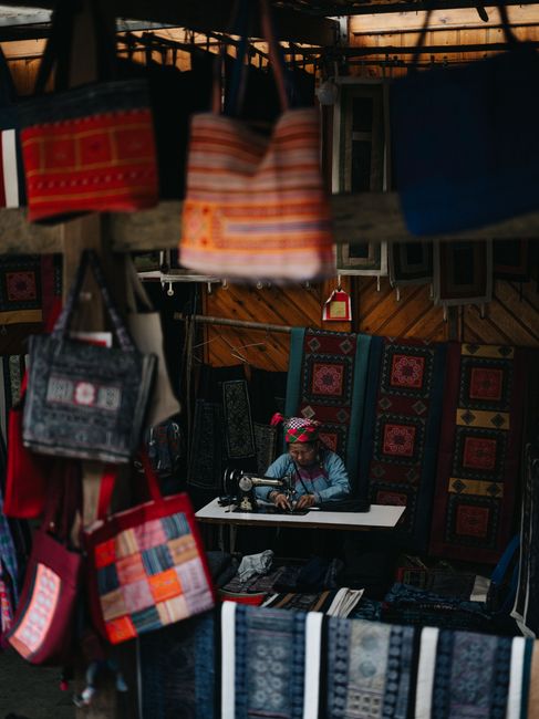 A vibrant scene of a traditional textile market in Lào Cai, showcasing handcrafted fabric and bags.