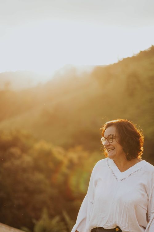 Free Smiling senior woman enjoying a beautiful sunset over lush countryside hills. Stock Photo
