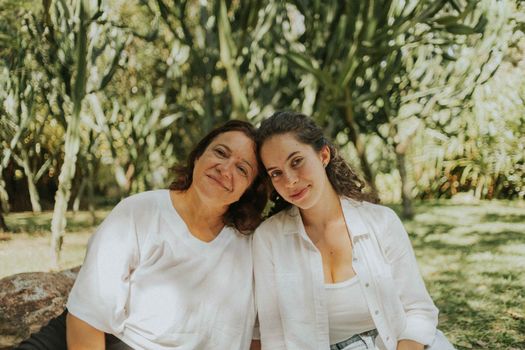 A mother and daughter enjoy a sunny day outdoors, sitting together in a lush garden.