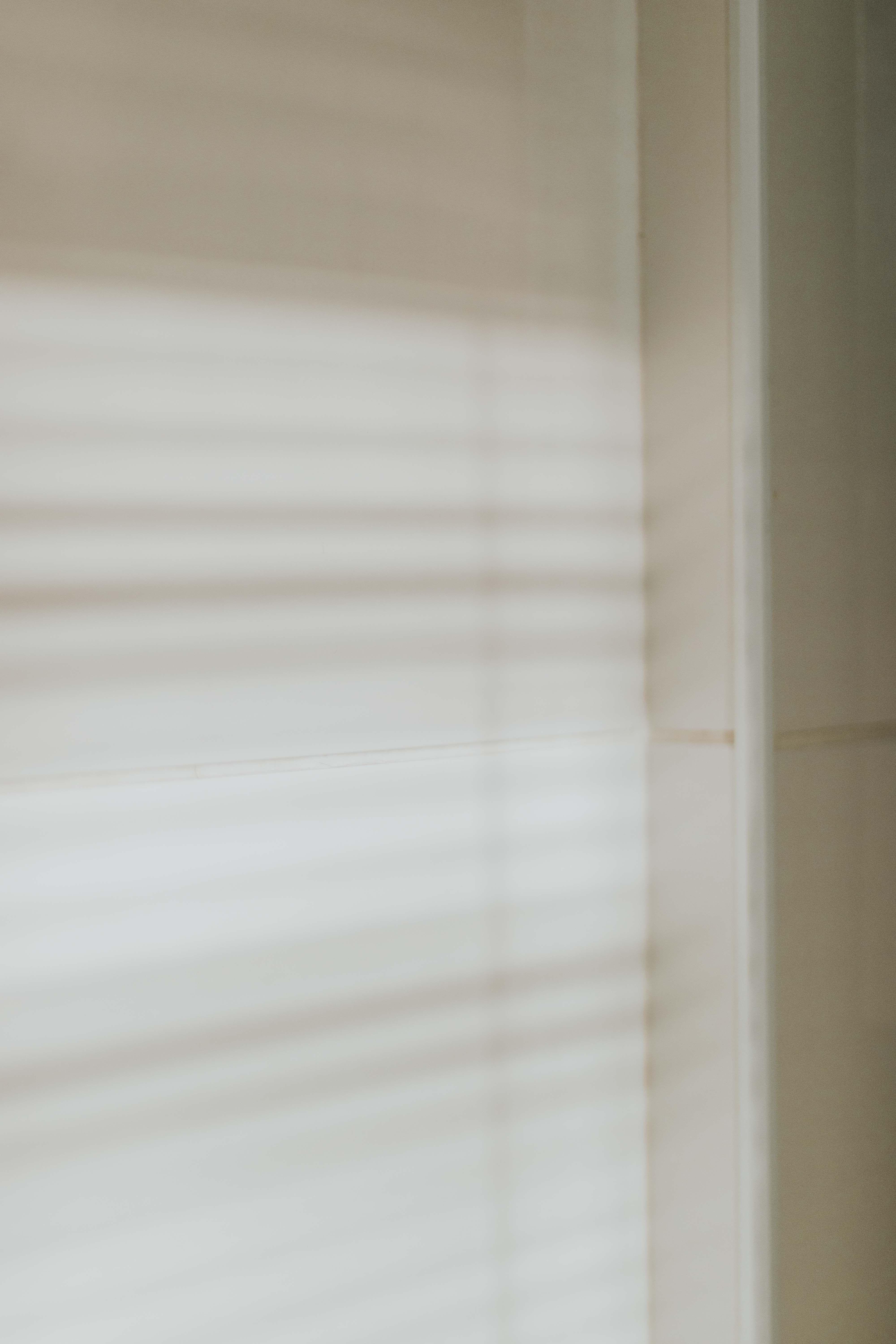 Soft shadows of blinds create a minimalist pattern on a beige wall, evoking a tranquil ambiance.