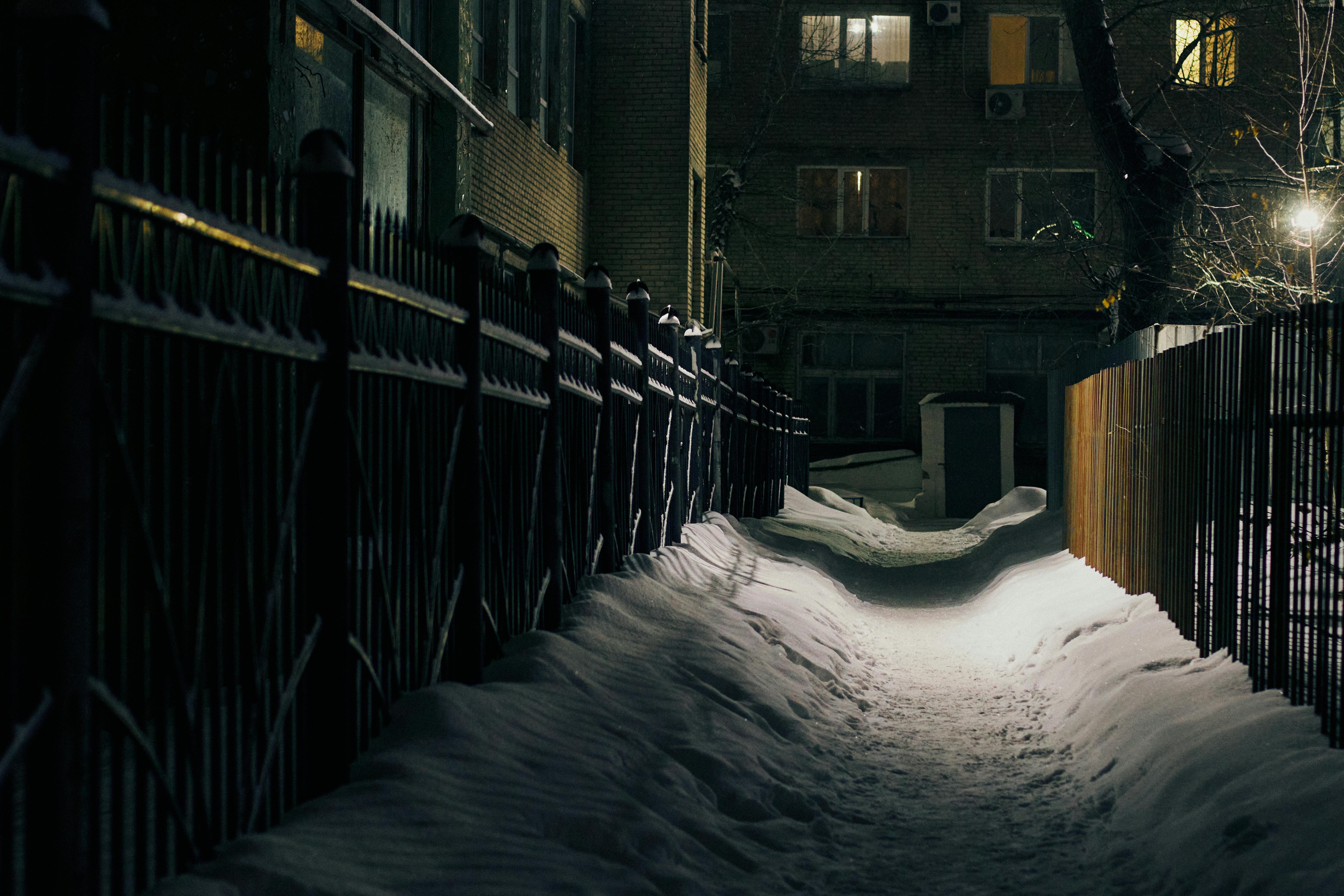 De franc Una escena nocturna d'hivern d'un carreró cobert de neu entre edificis amb tanques i llums. Foto d'estoc