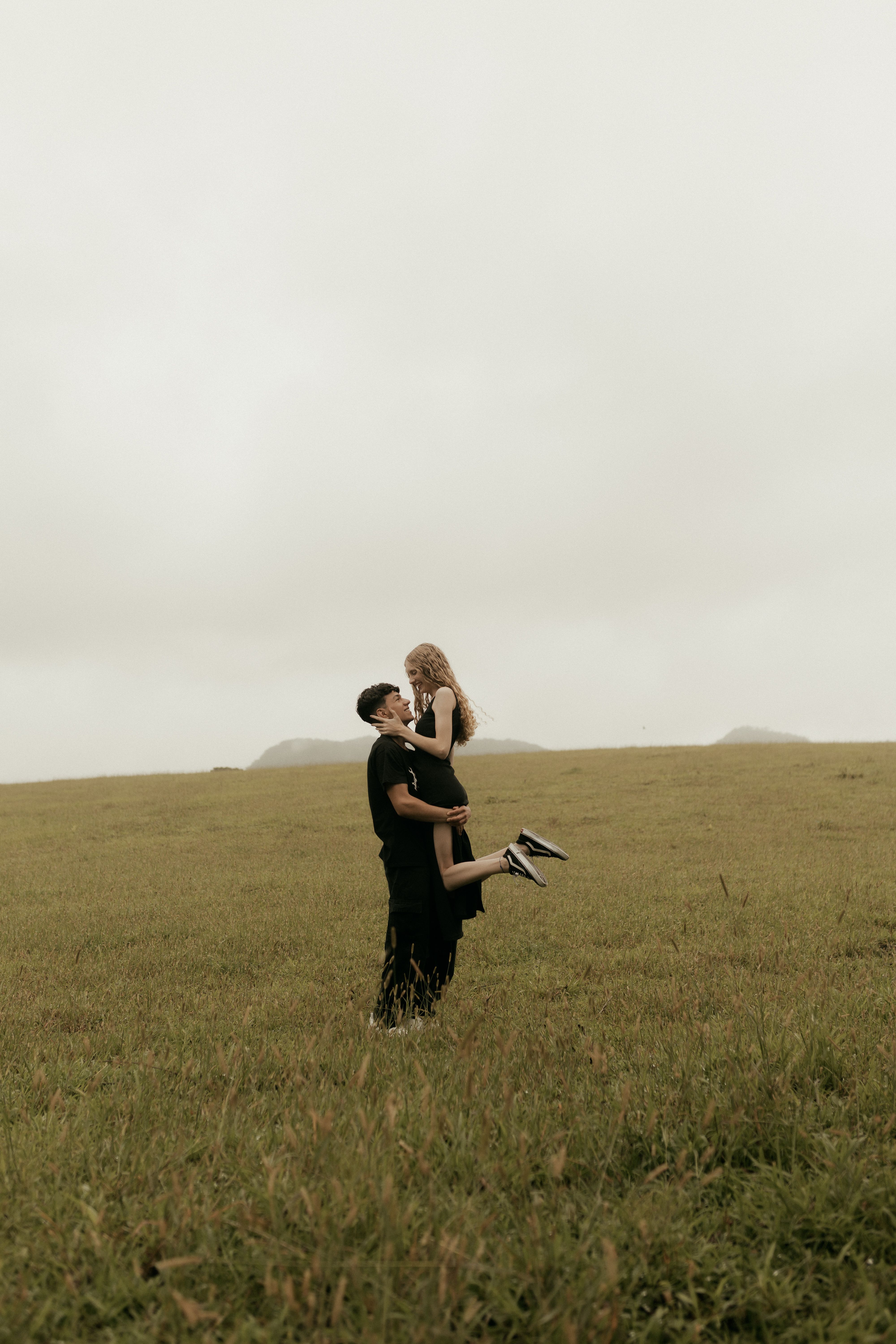 Young couple embracing in peaceful meadow under overcast sky, expressing love and connection.