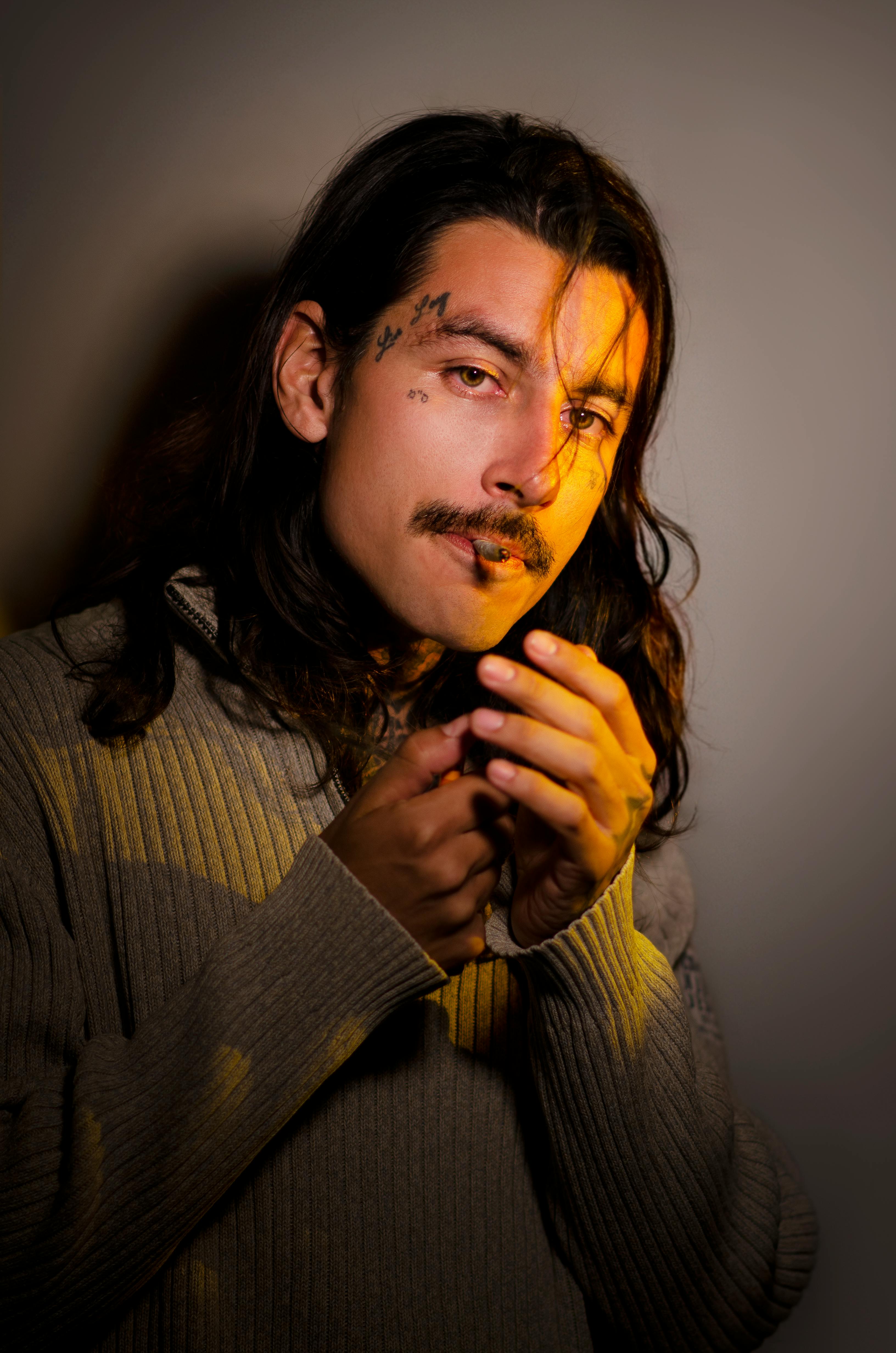 Gratis Ritratto ravvicinato di un uomo con tatuaggi sul viso, luci soffuse che creano un'atmosfera misteriosa. Foto a disposizione