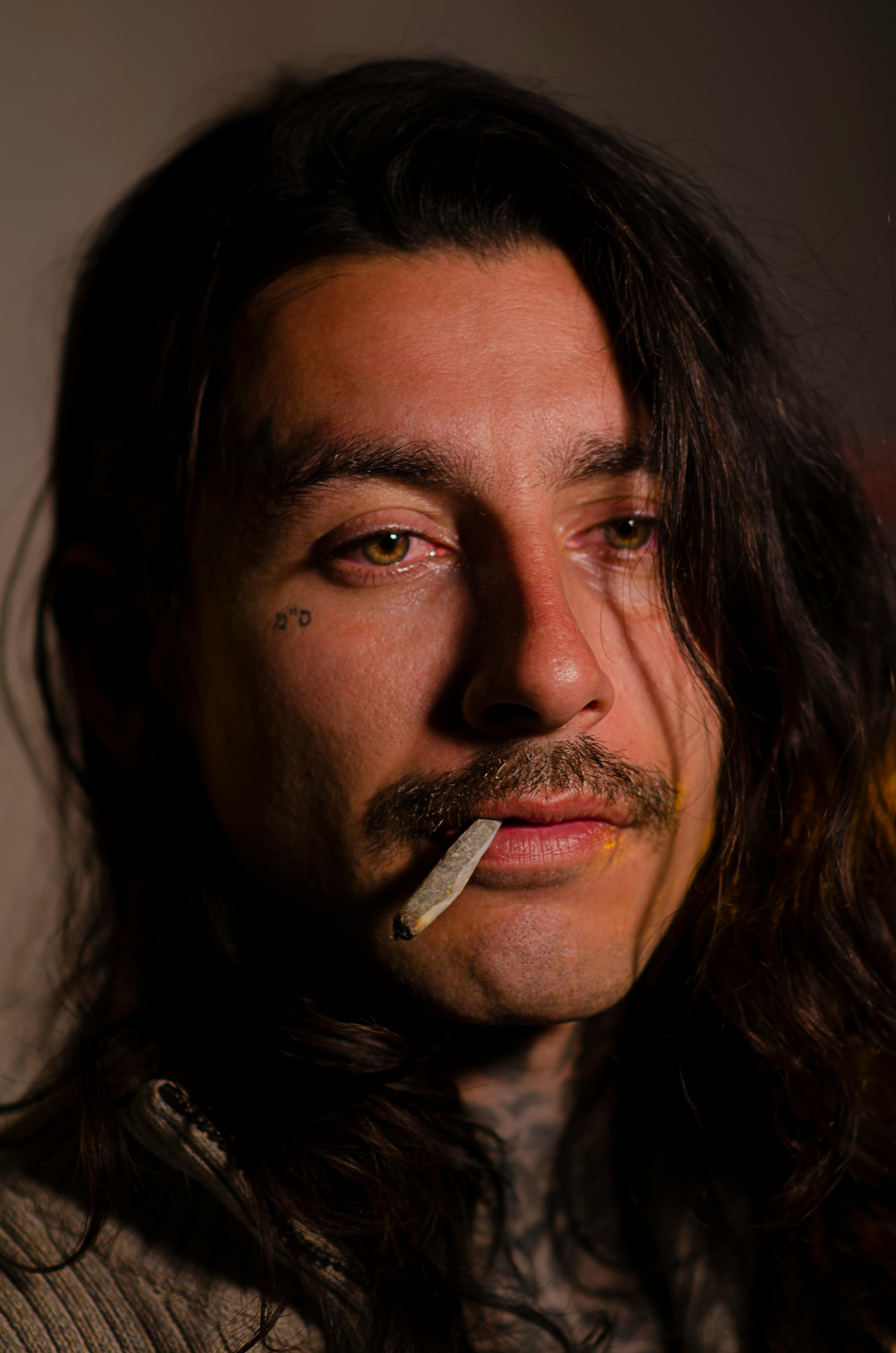 Free Moody close-up portrait of a man with tattoos and a cigarette. Intimate and dramatic lighting. Stock Photo