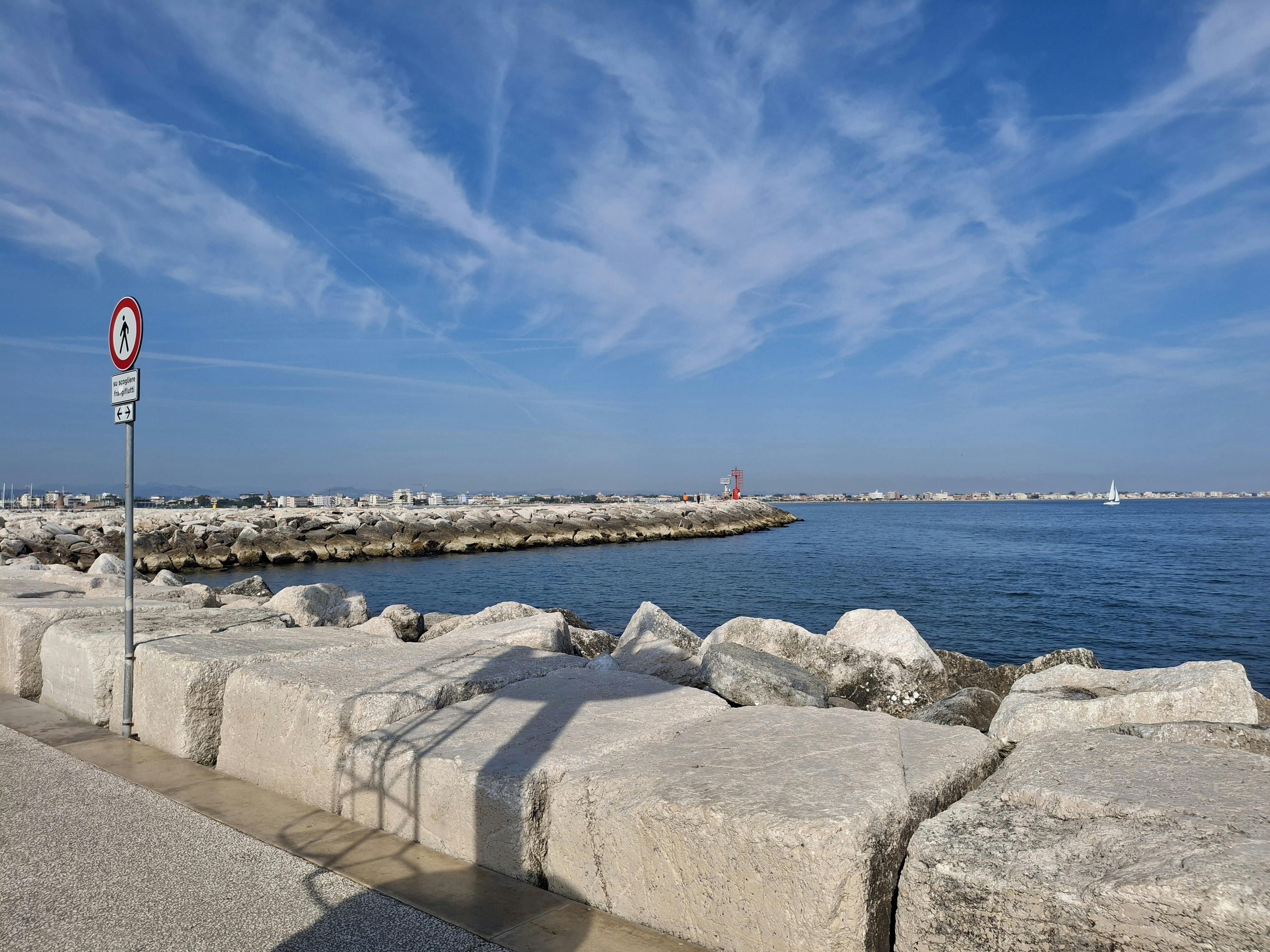 無料 澄み切った青空の下、岩の多い防波堤が広がる静かな海辺の景色。旅行や自然コンテンツに最適です。 写真素材