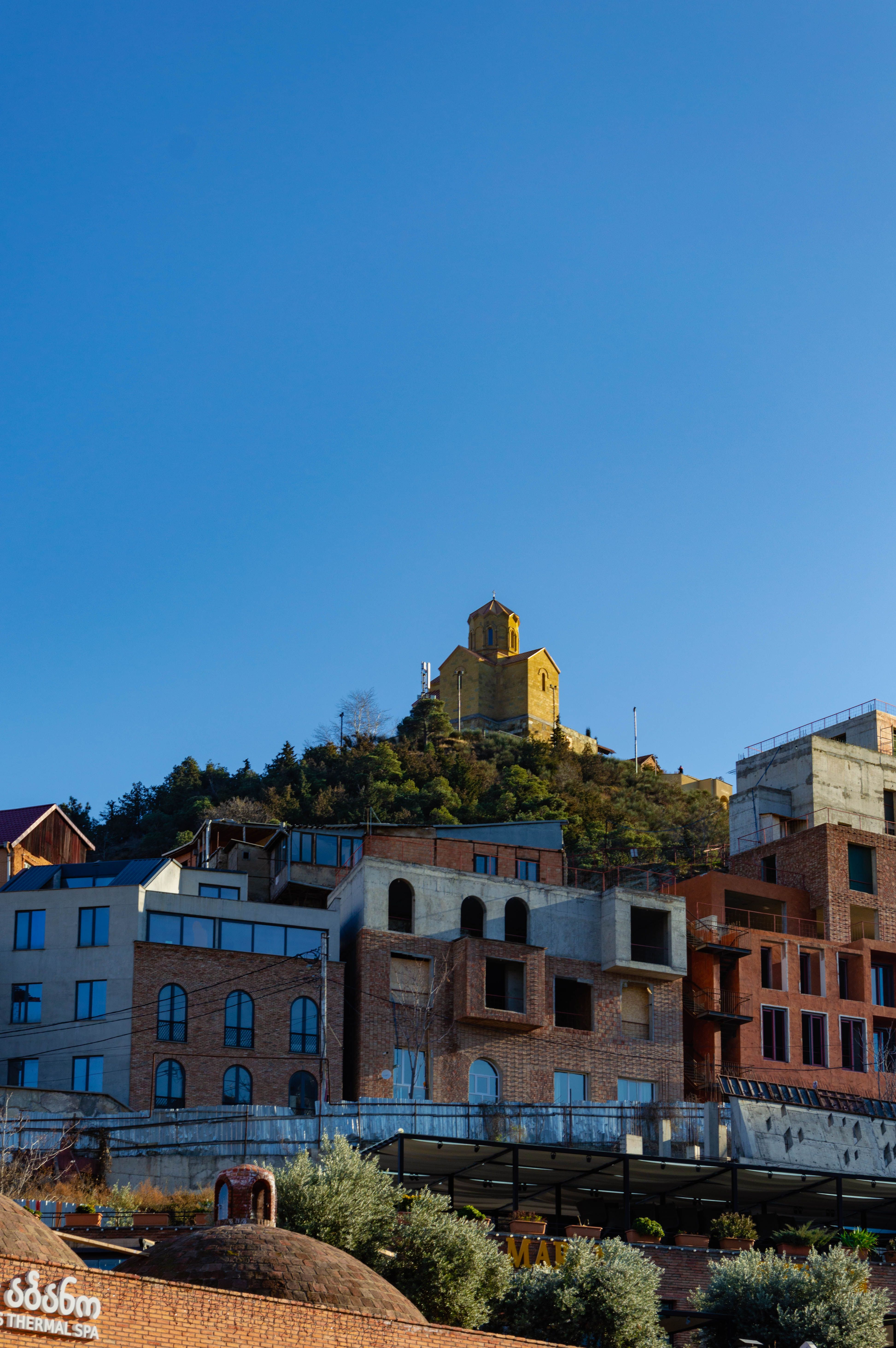 A picturesque view of Tbilisi architecture with a church on a hill under a clear blue sky.