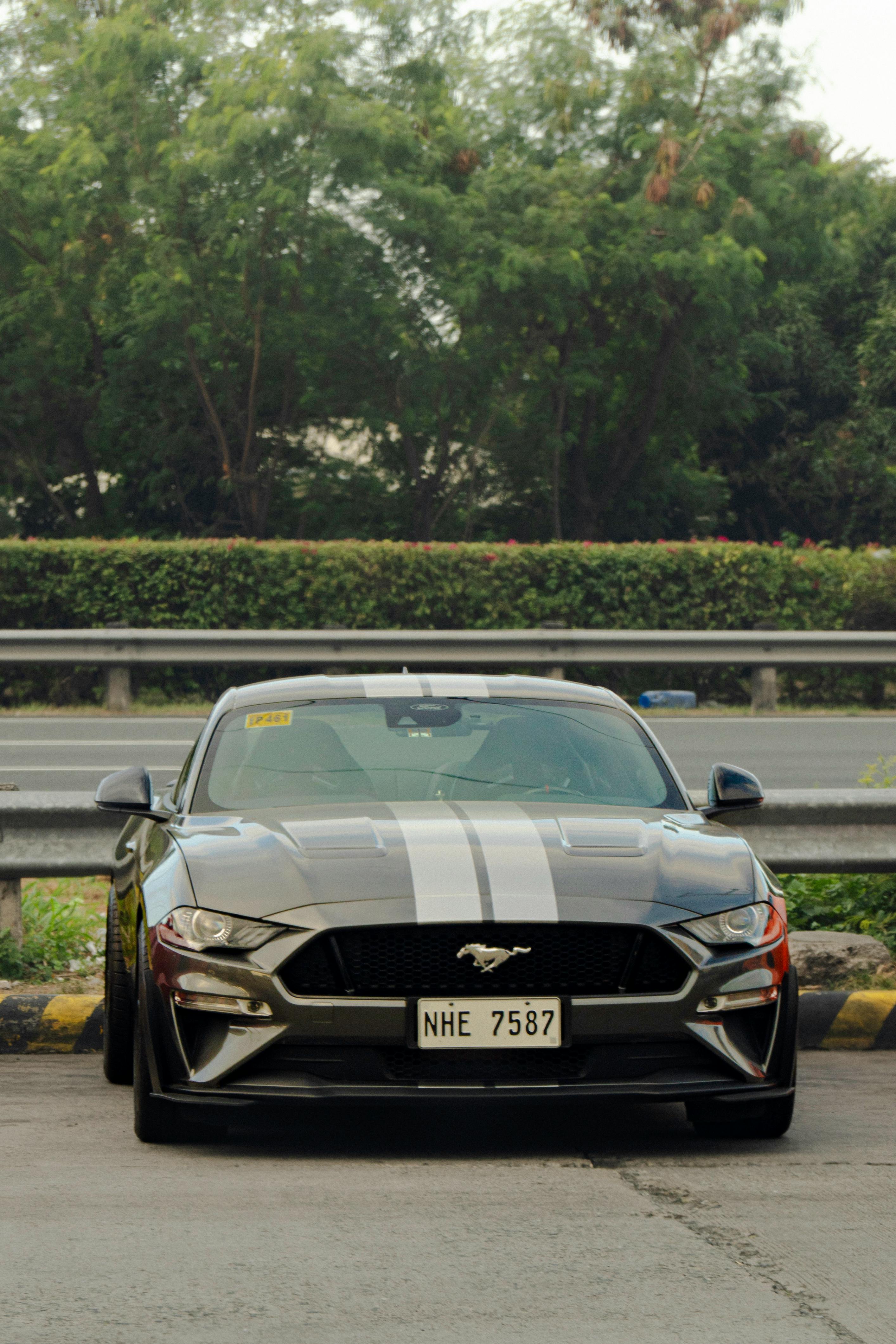 бесплатная Вид спереди на черный спортивный автомобиль, припаркованный на шоссе, на заднем плане видны деревья. Стоковое фото