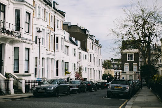 Street view of classic white townhouses and parked cars on a peaceful city road.