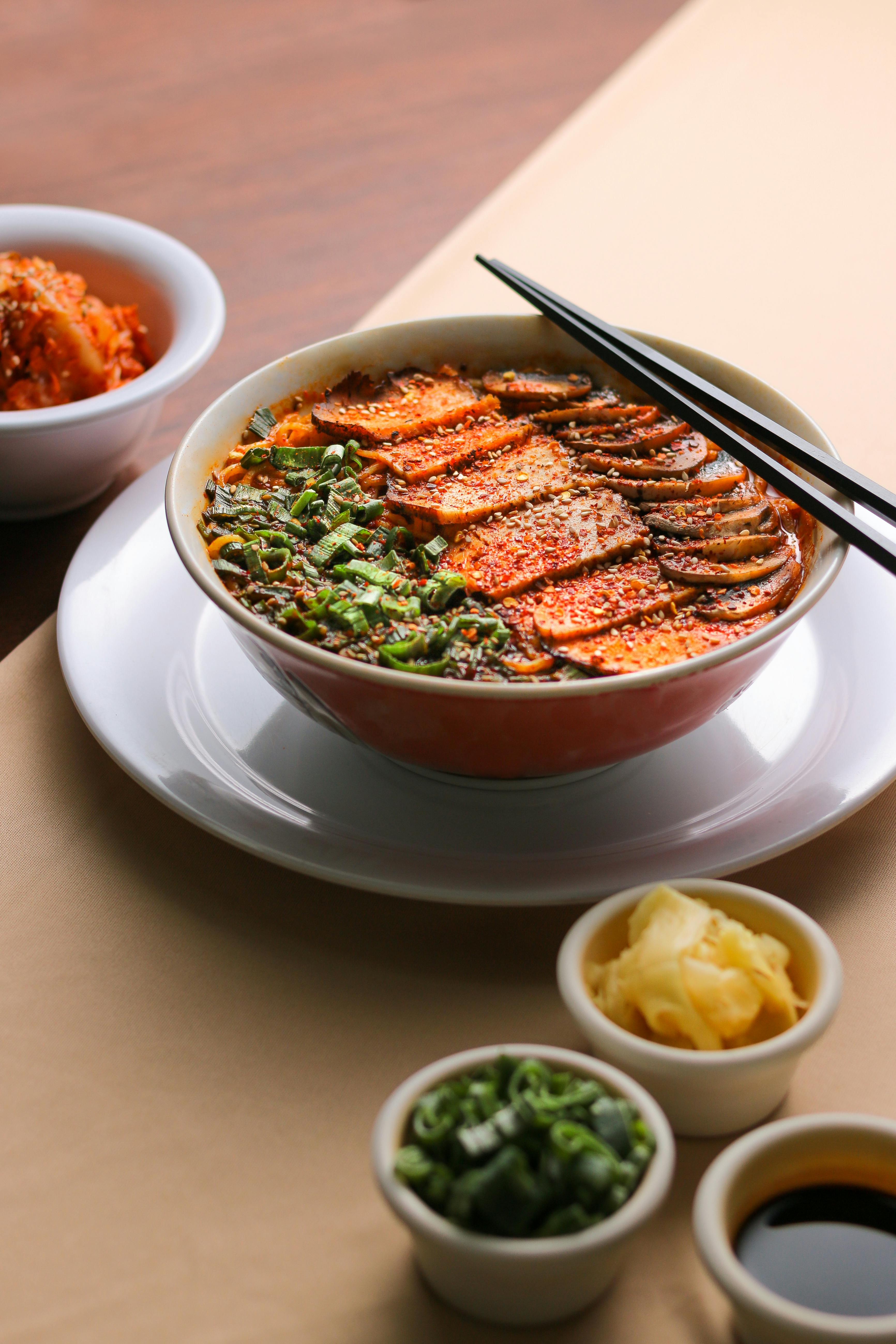 бесплатная Насладитесь этой великолепно оформленной порцией рамена со свежими добавками и палочками для еды — идеальный вариант для любителей азиатской кухни. Стоковое фото